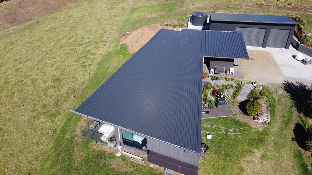 An Aerial View of a House With a Black Roof in a Grassy Field — Beards Roofing and Plumbing in Bribie Island, QLD