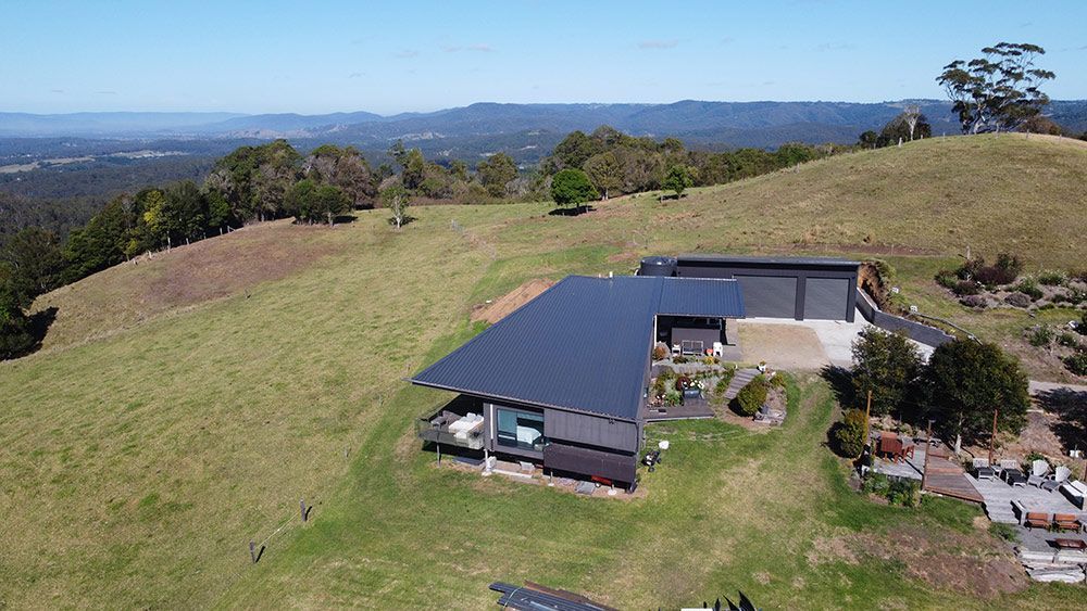 An Aerial View of a House on Top of a Grassy Hill — Beards Roofing and Plumbing in Clontarf, QLD