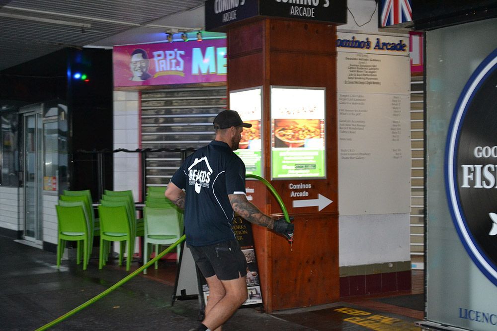 A Man is Cleaning the Outside of a Restaurant With a Hose — Beards Roofing and Plumbing in Clontarf, QLD
