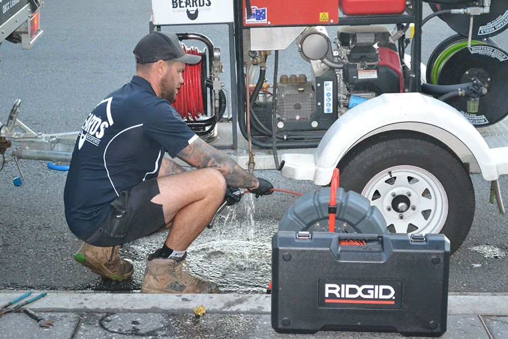 A Man is Kneeling Down Next to a Toolbox That Says Ridgid on It — Beards Roofing and Plumbing in Bribie Island, QLD