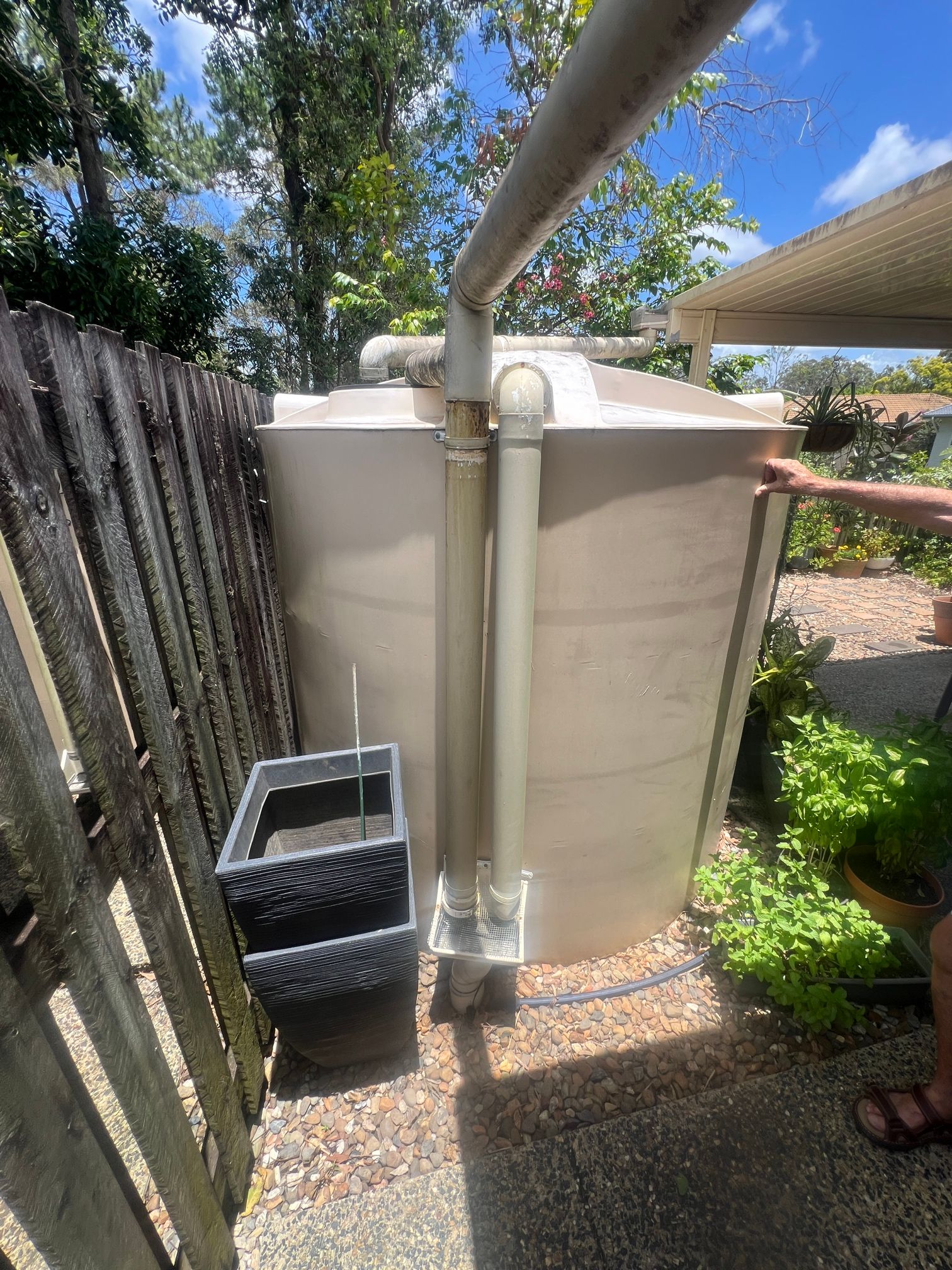 Water Tank is Sitting Next to a Wooden Fence — Beards Roofing and Plumbing in Clontarf, QLD