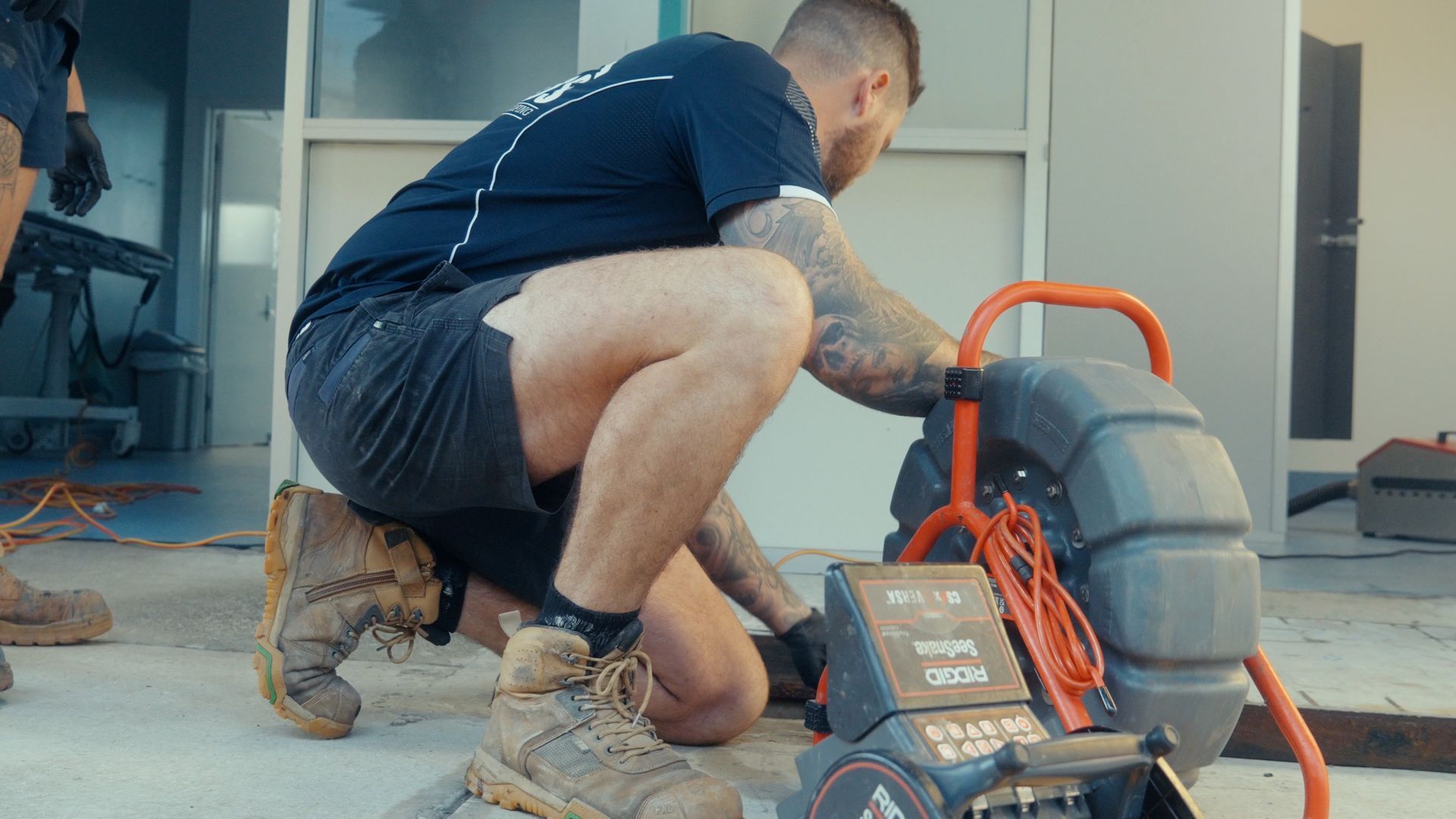 Man is Kneeling Down Next to a Machine — Beards Roofing and Plumbing in Clontarf, QLD