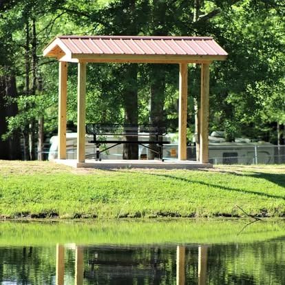 A wooden gazebo with a metal roof sits next to a body of water