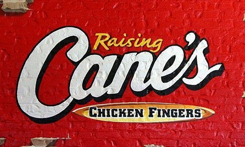 A red brick wall with raising cane 's chicken fingers written on it