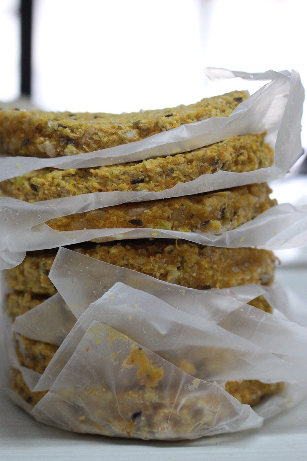 Pila de productos horneados redondos, de color dorado, posiblemente galletas o barras, envueltos en papel pergamino blanco.
