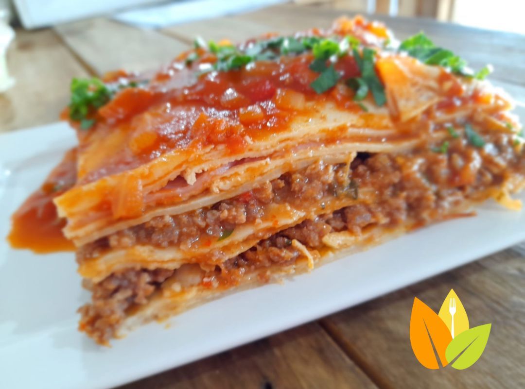 Rebanada de plato en capas con relleno de carne, salsa roja y hierbas sobre un plato blanco.
