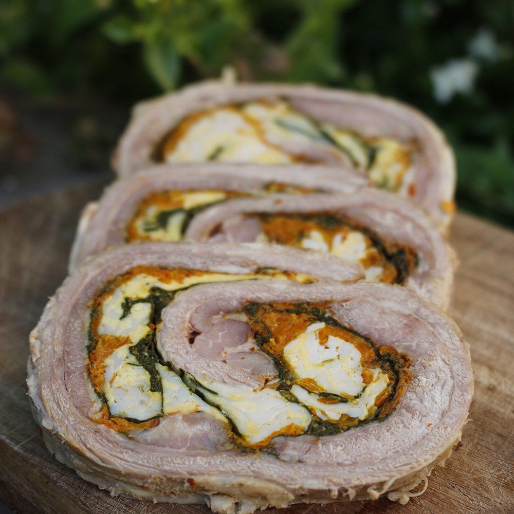 Carne enrollada en rodajas con un vibrante relleno de naranja y verde sobre una tabla de madera.