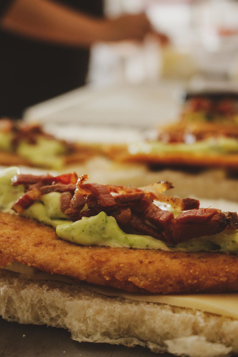 Primer plano de un sándwich con una chuleta frita, crema de aguacate y tocino en un panecillo.