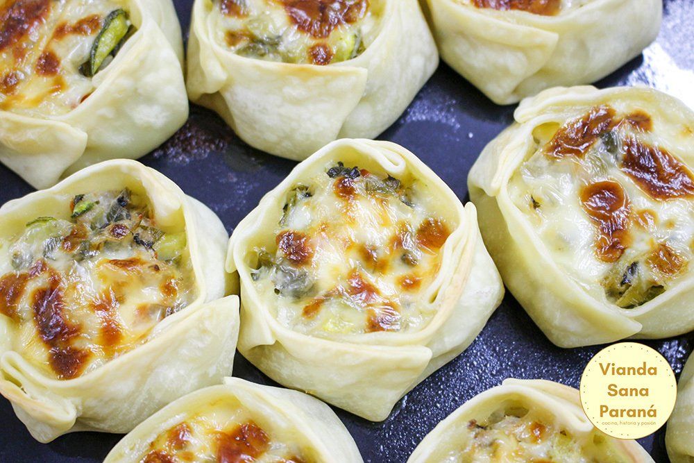 Pasteles horneados rellenos de verduras y queso, dispuestos sobre una superficie oscura.