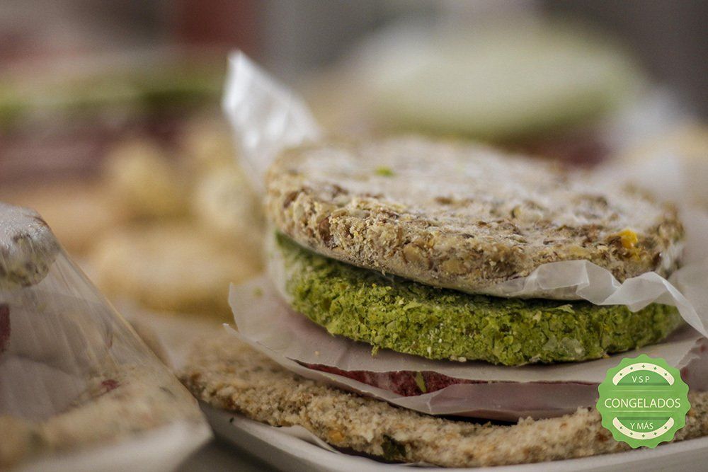 Sandwich with green patty and grainy bread on white paper.