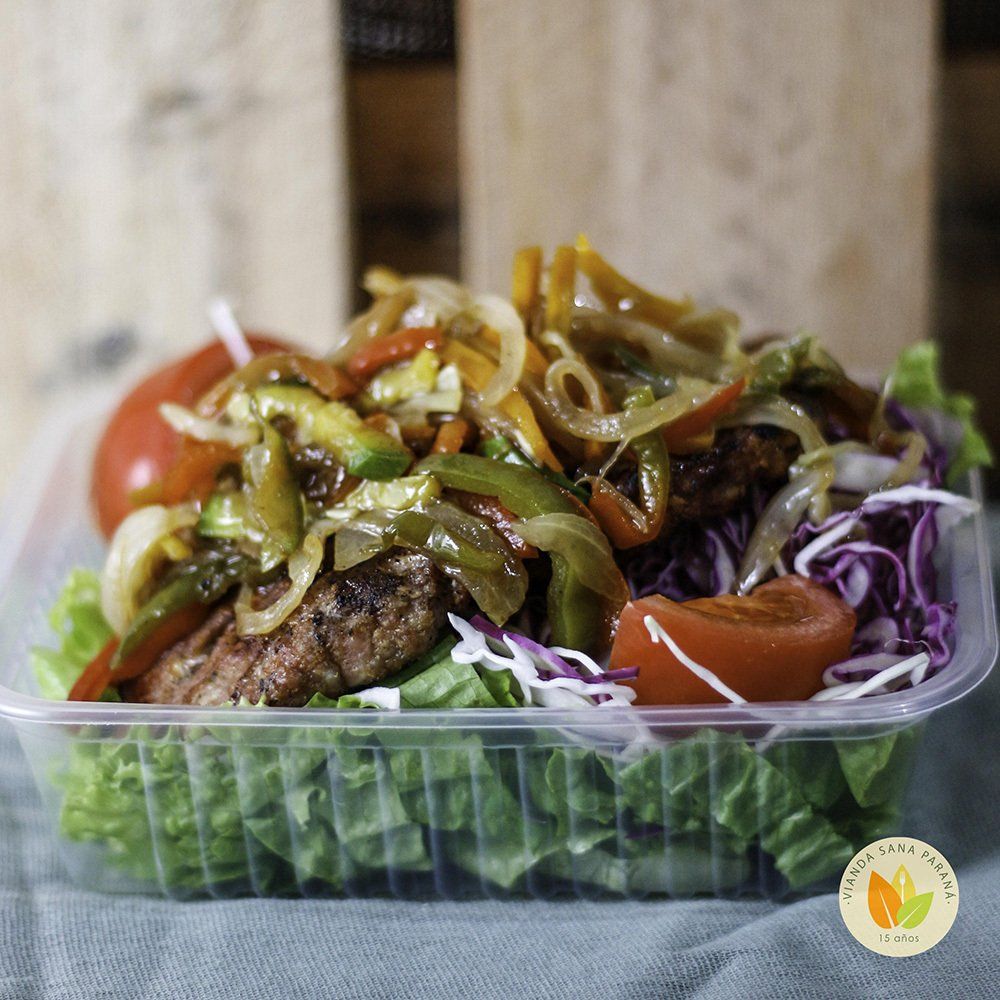 Ensalada con carne a la parrilla, pimientos y cebollas salteados en un recipiente de plástico transparente.
