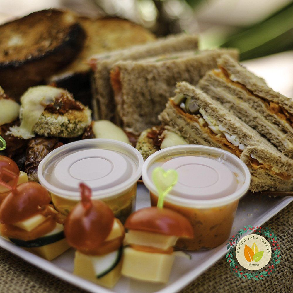 Primer plano de un plato cuadrado con sándwiches pequeños, brochetas de aperitivo, tazas de sopa y pan tostado.