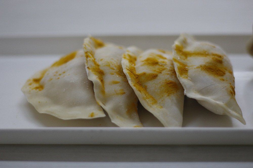 Cuatro albóndigas sobre un plato rectangular blanco, en primer plano. Son de color blanquecino con los bordes dorados.
