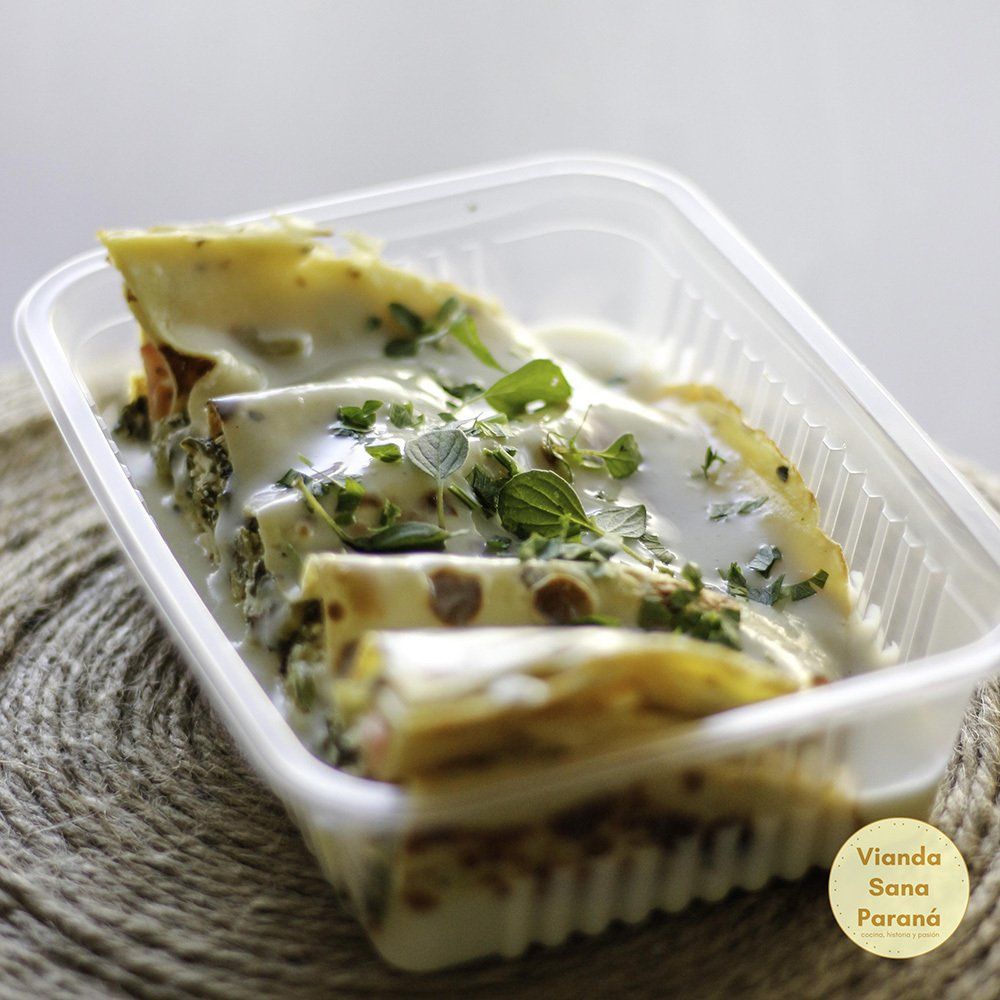 Pasta en salsa blanca con hierbas en un recipiente de plástico transparente.