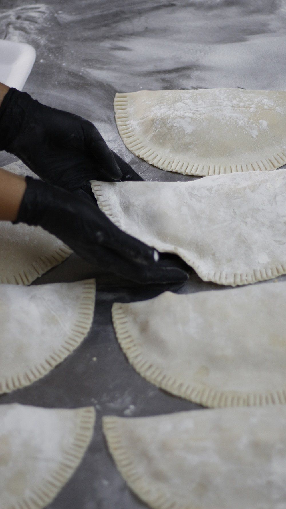 Hands in black gloves arranging pastry-like turnovers on a floured surface.