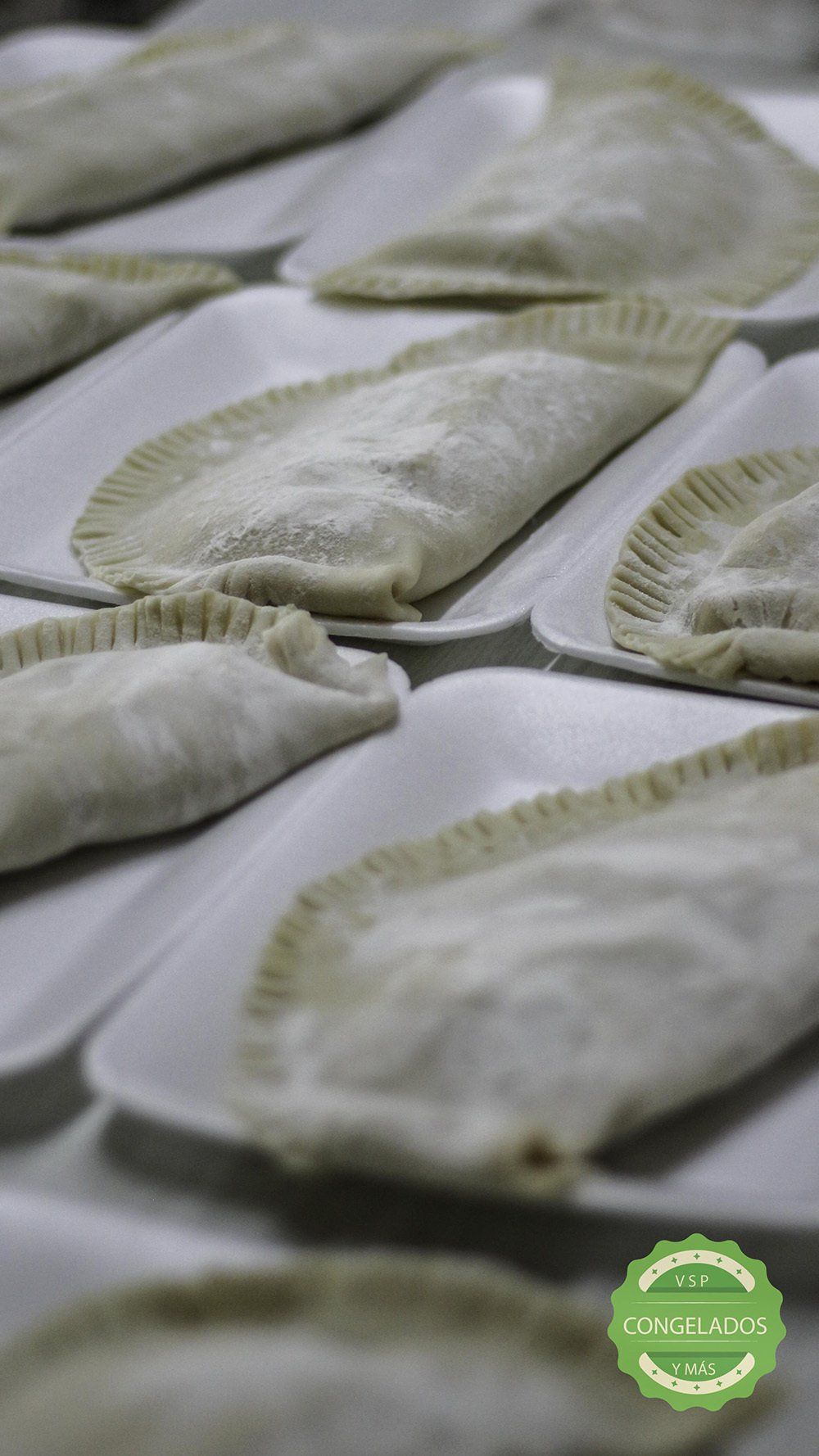 Varios pasteles crudos, con los bordes redondeados, sobre bandejas blancas.