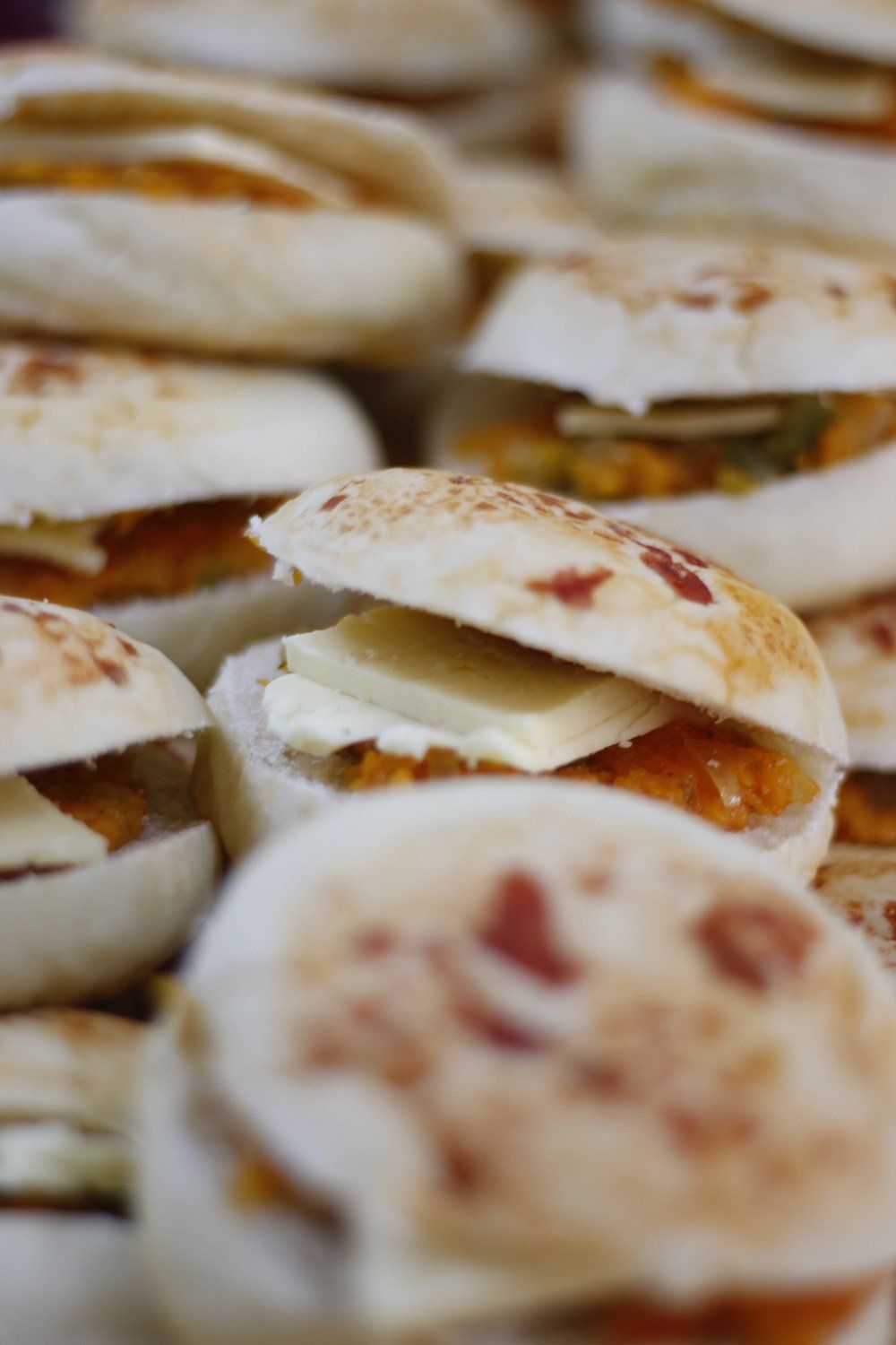 Miniature sandwiches, close-up. White bread rolls with various fillings, including cheese and orange-colored spread.