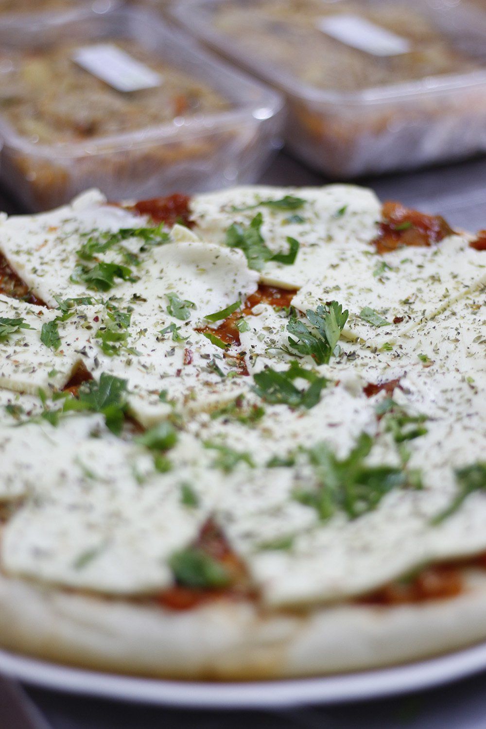 Pizza con queso blanco, salsa de tomate y hierbas frescas en un plato blanco. Otros recipientes de comida se ven al fondo.