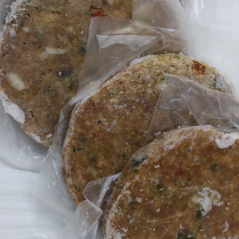 Hamburguesas congeladas en envase de plástico transparente, con hierbas y especias visibles.