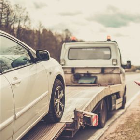 A white car is being towed by a tow truck