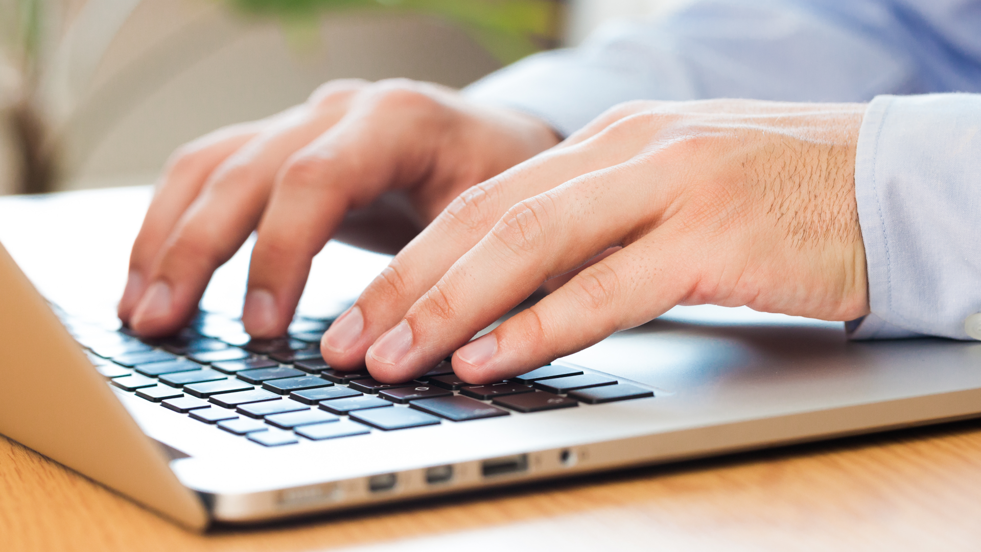 A man is typing on a laptop computer on a wooden table.
