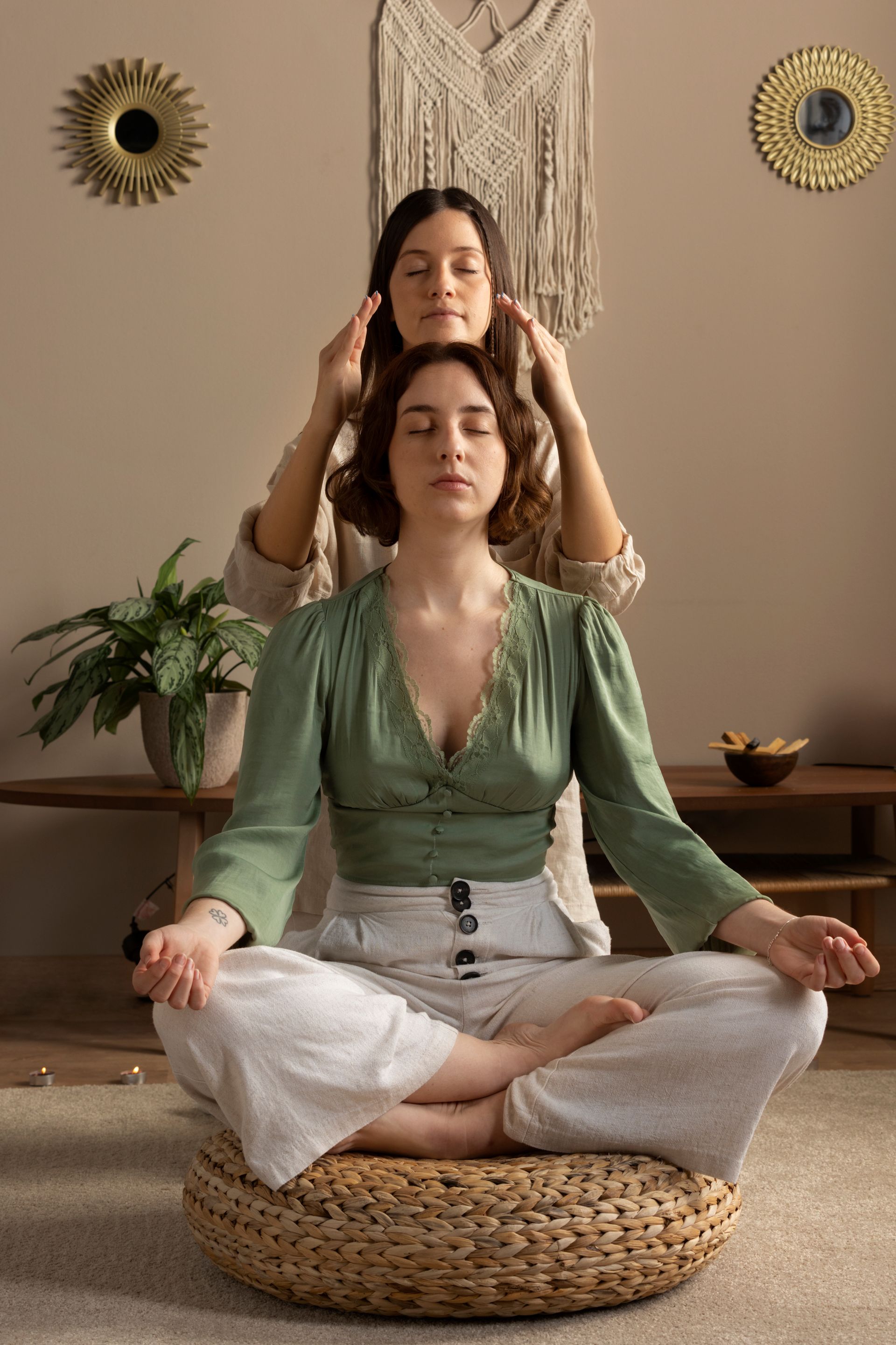 A woman is sitting in a lotus position while another woman massages her head.