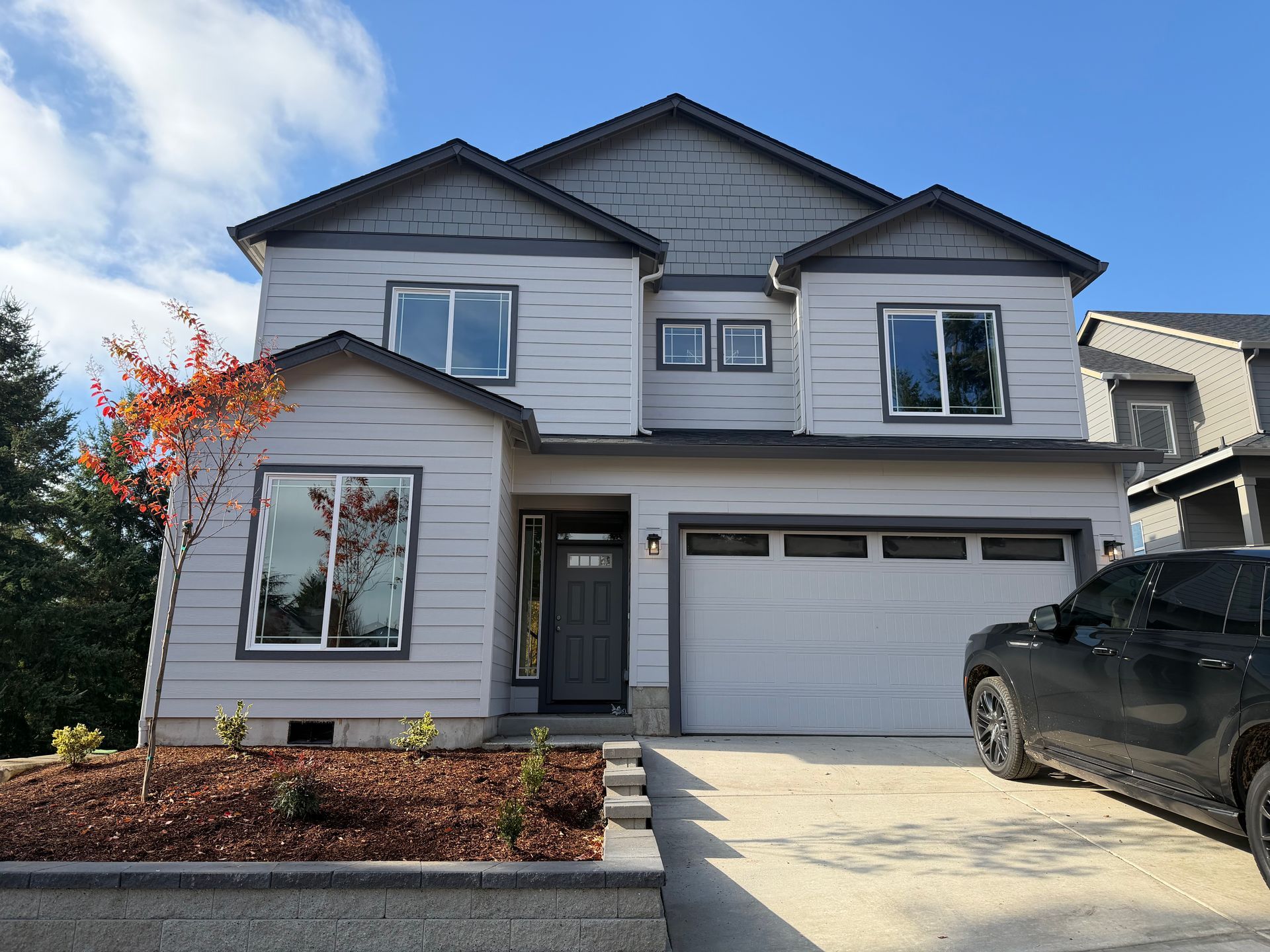 Two-story gray house with white garage door and black SUV parked in driveway under blue sky.