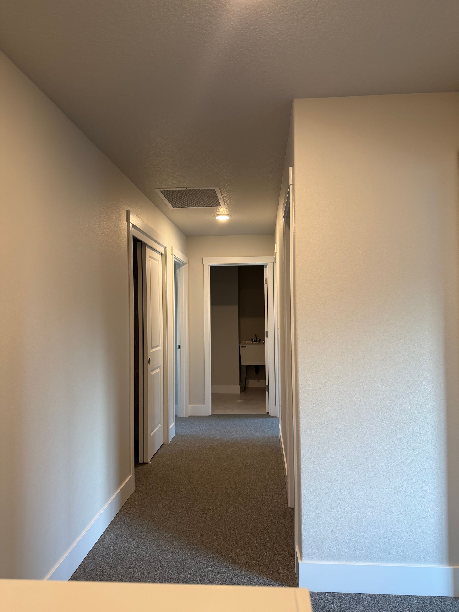 A narrow hallway with carpet, white walls and doors, leading to a bathroom.