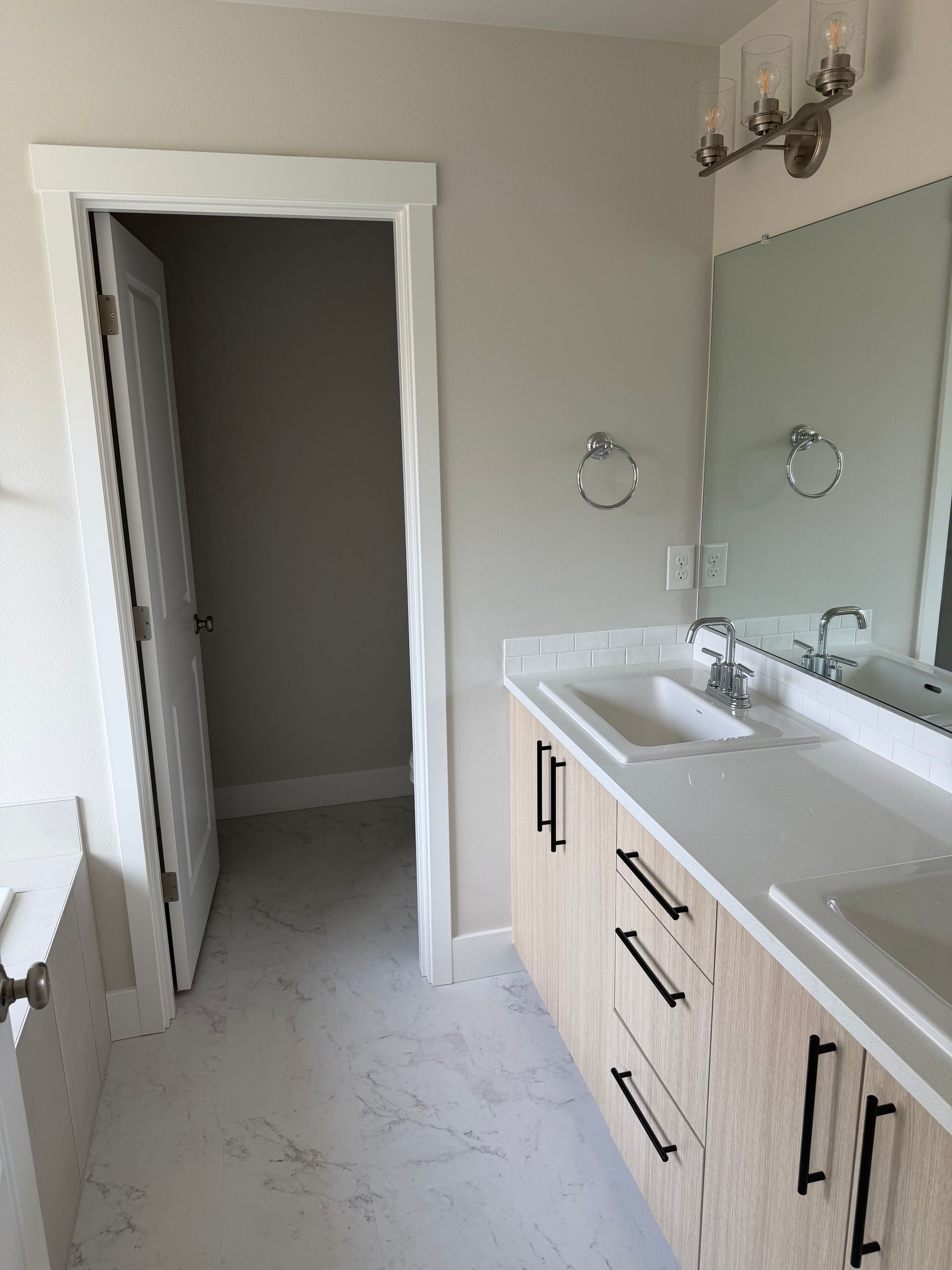 Bathroom with light wood vanity, white countertops, and open door to a closet.