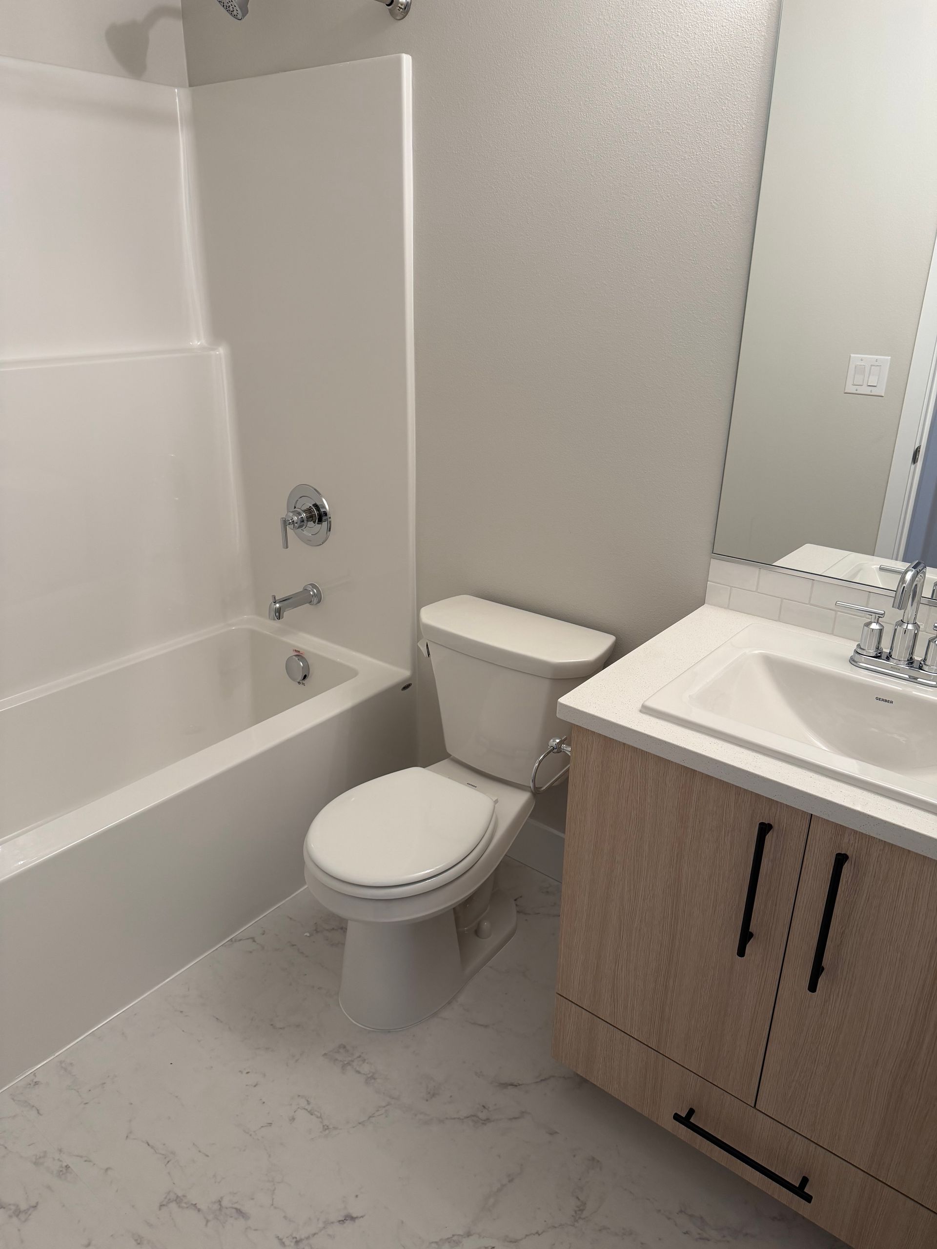 Bathroom with white tub, toilet, and vanity with a light wood cabinet, and light-colored tile.