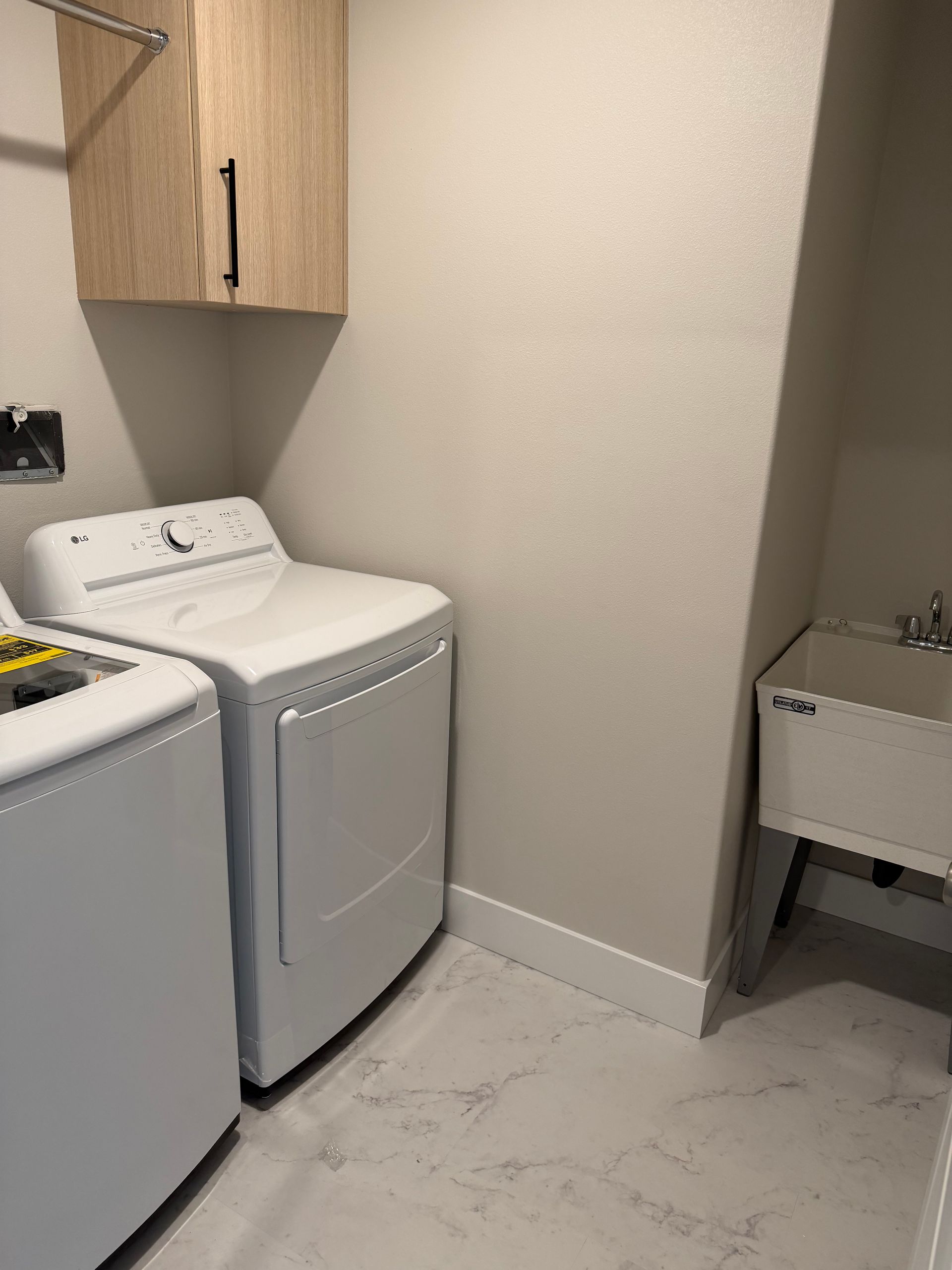 Laundry room with white appliances, light wood cabinets, and a utility sink.