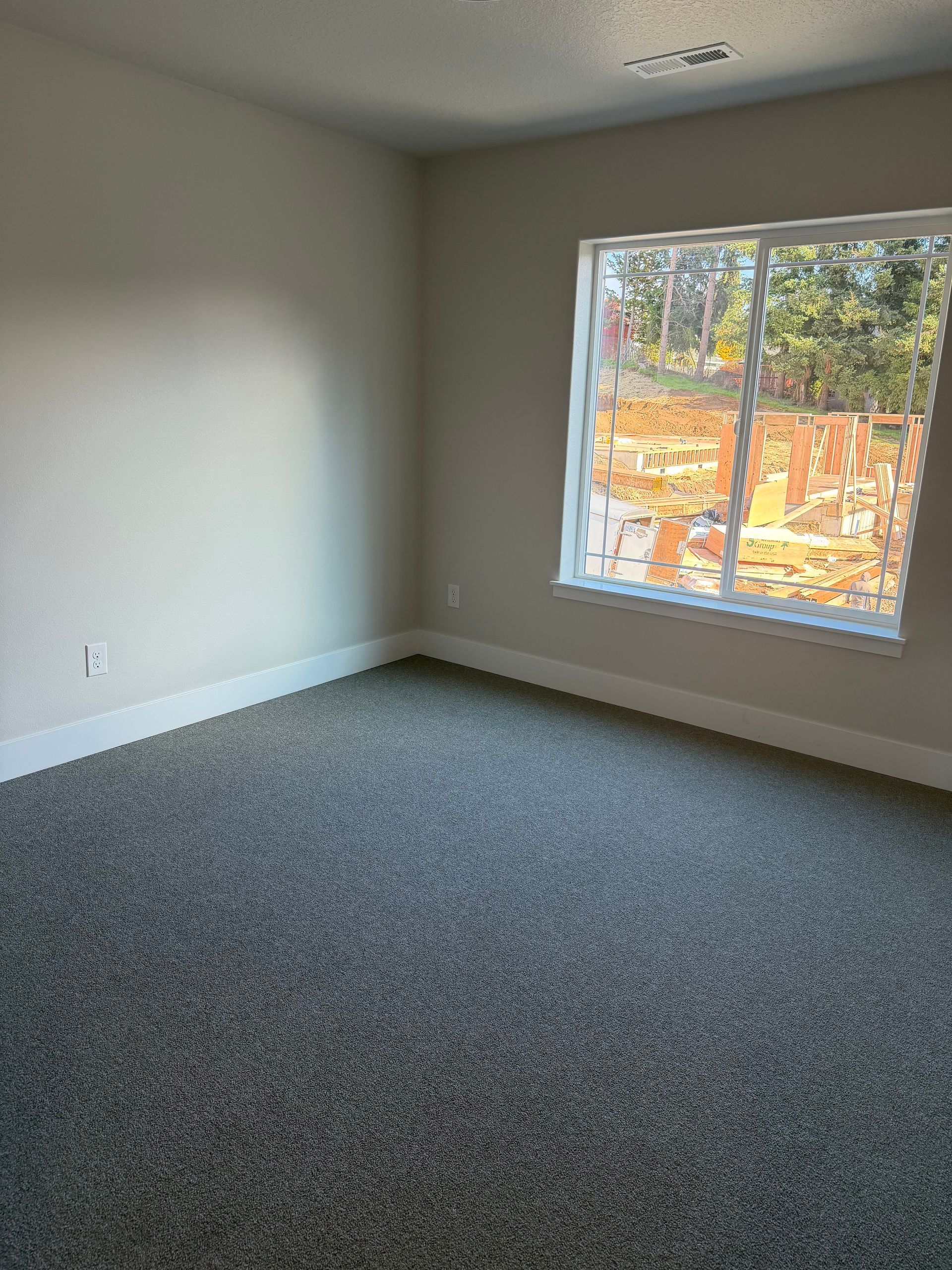 Empty room with gray carpet and walls, a window showing a bright outdoors.