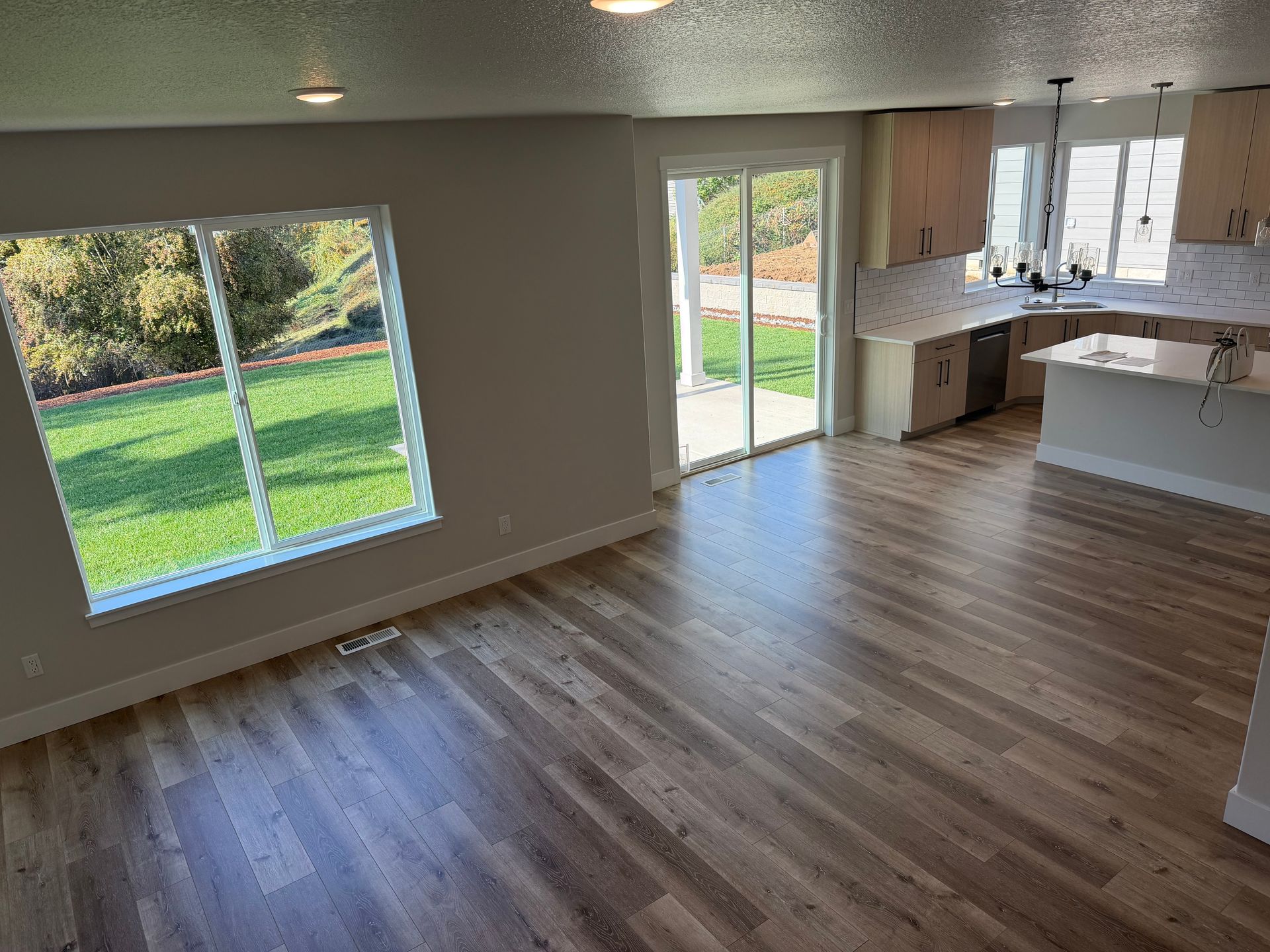 Interior of a home with a large window and sliding glass door, hardwood floors, and a kitchen.