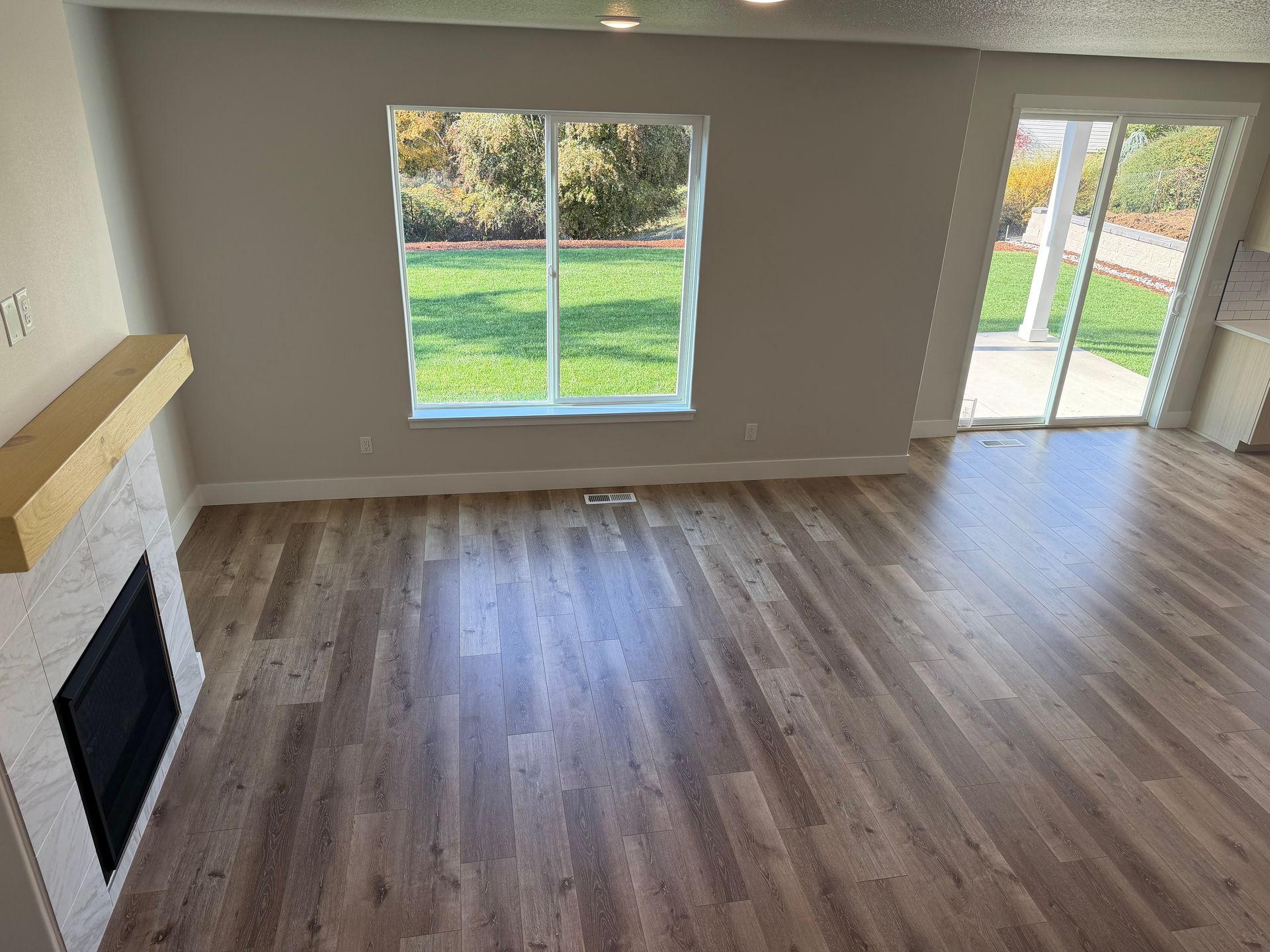 Living room with fireplace, window, and sliding glass door. Hardwood floor. Green lawn visible outside.