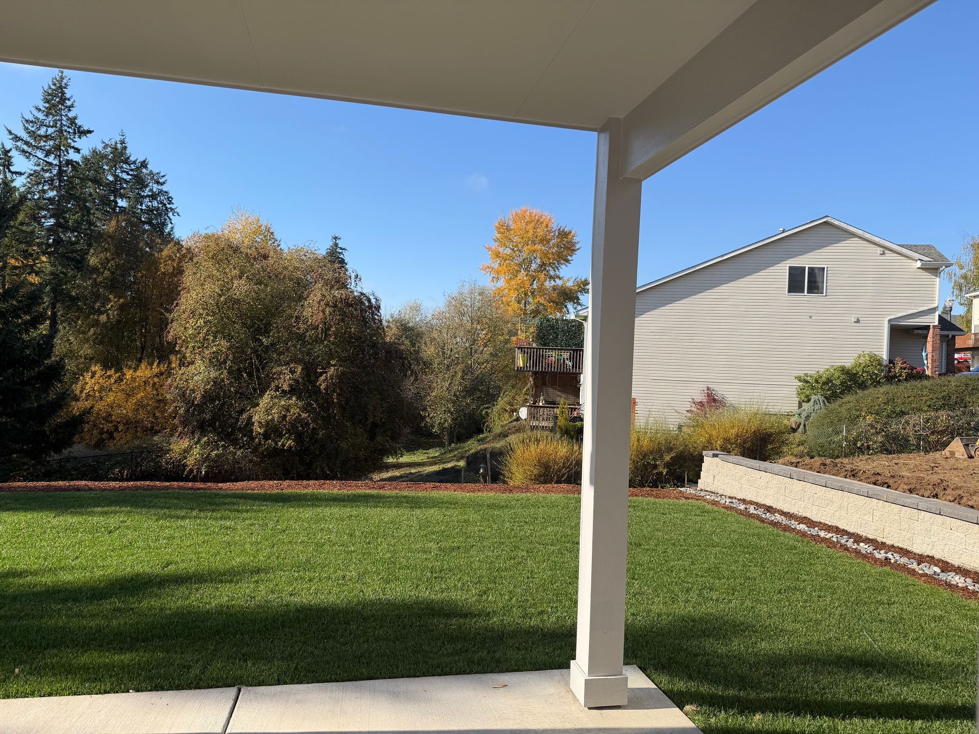 View from a porch of a green lawn, trees with fall foliage, and a house under a blue sky.