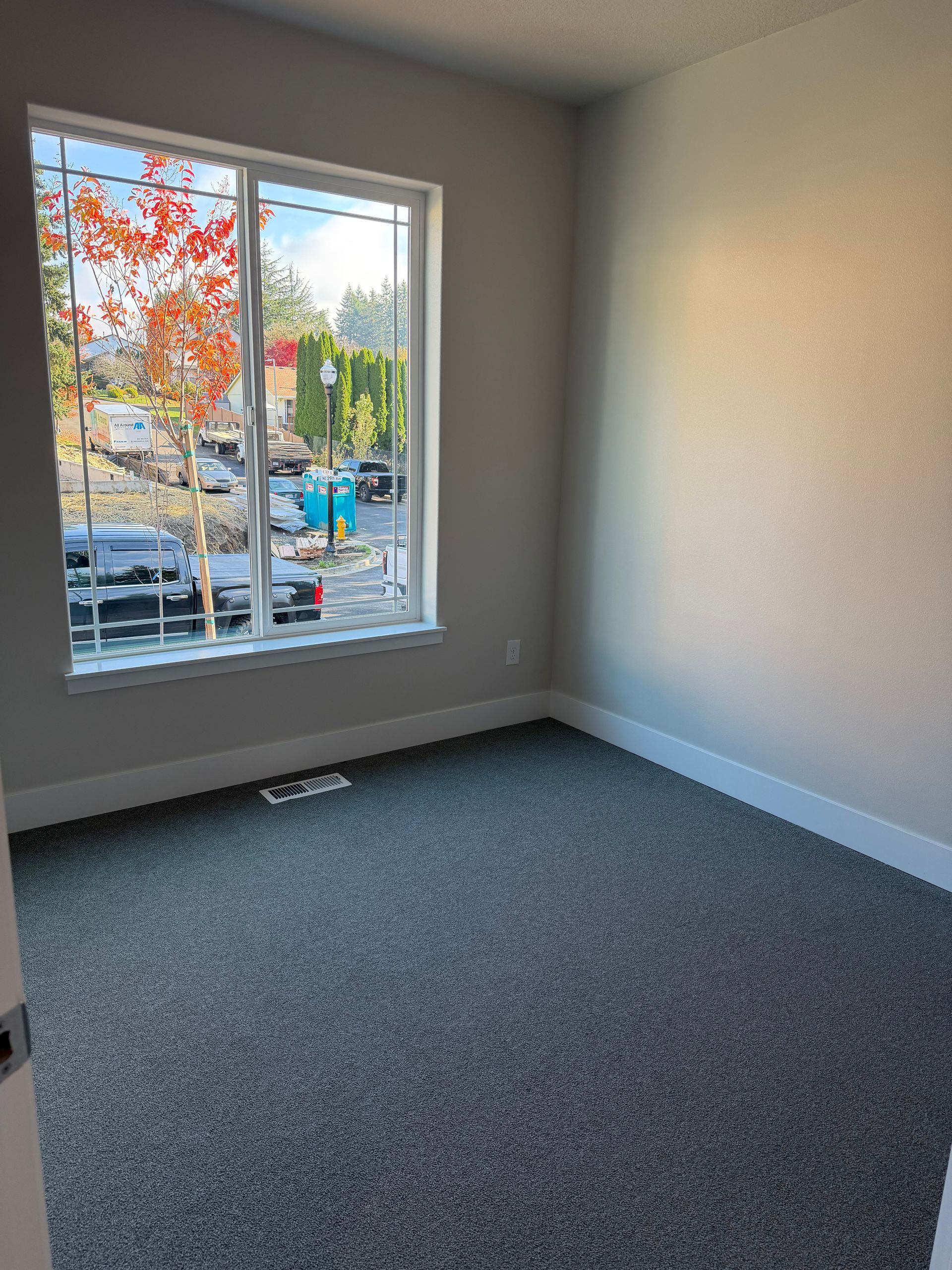 Empty room with gray carpet, window with view of street and trees.