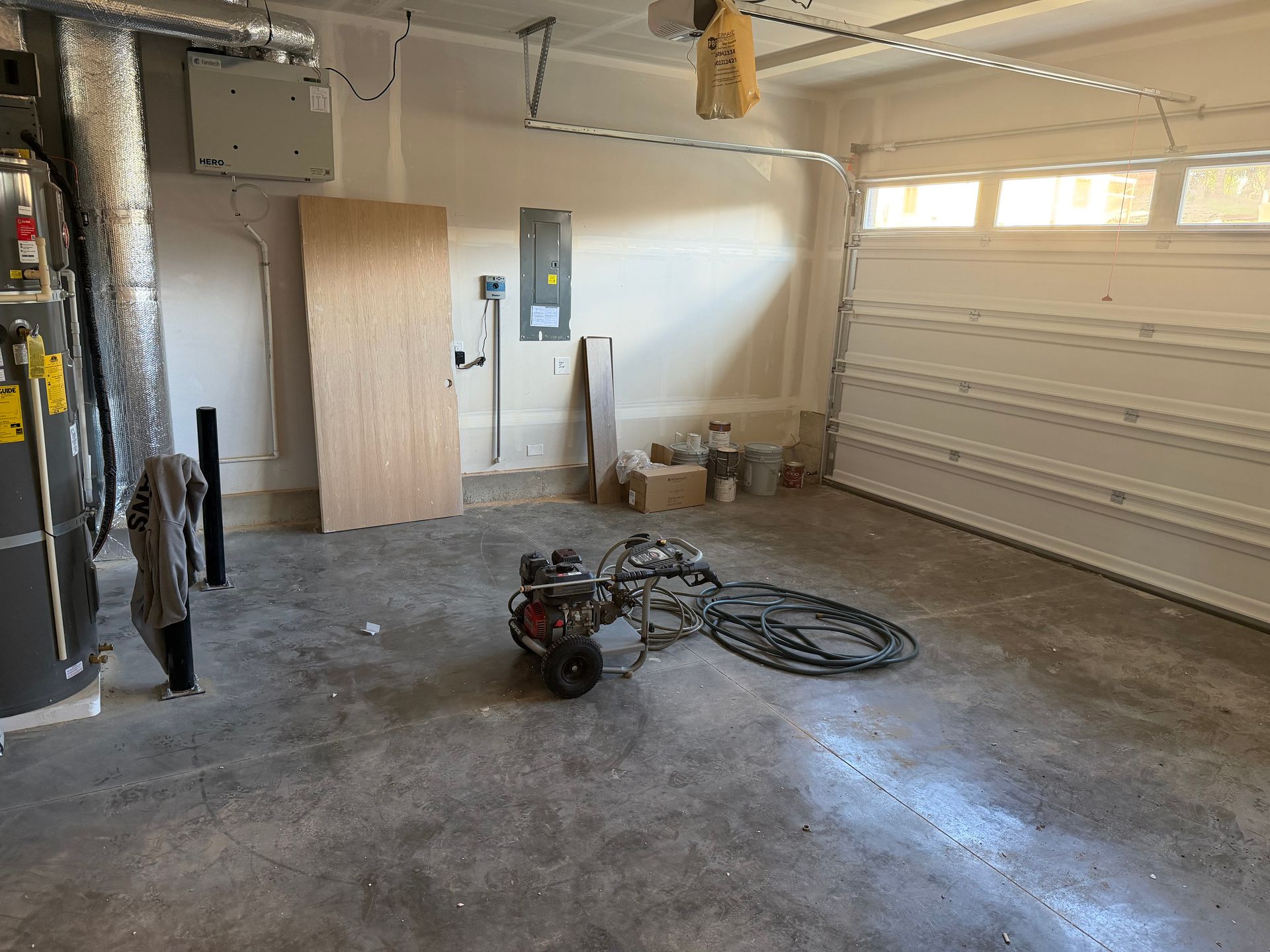 Unfinished garage interior with concrete floor, tools, and a closed white garage door.