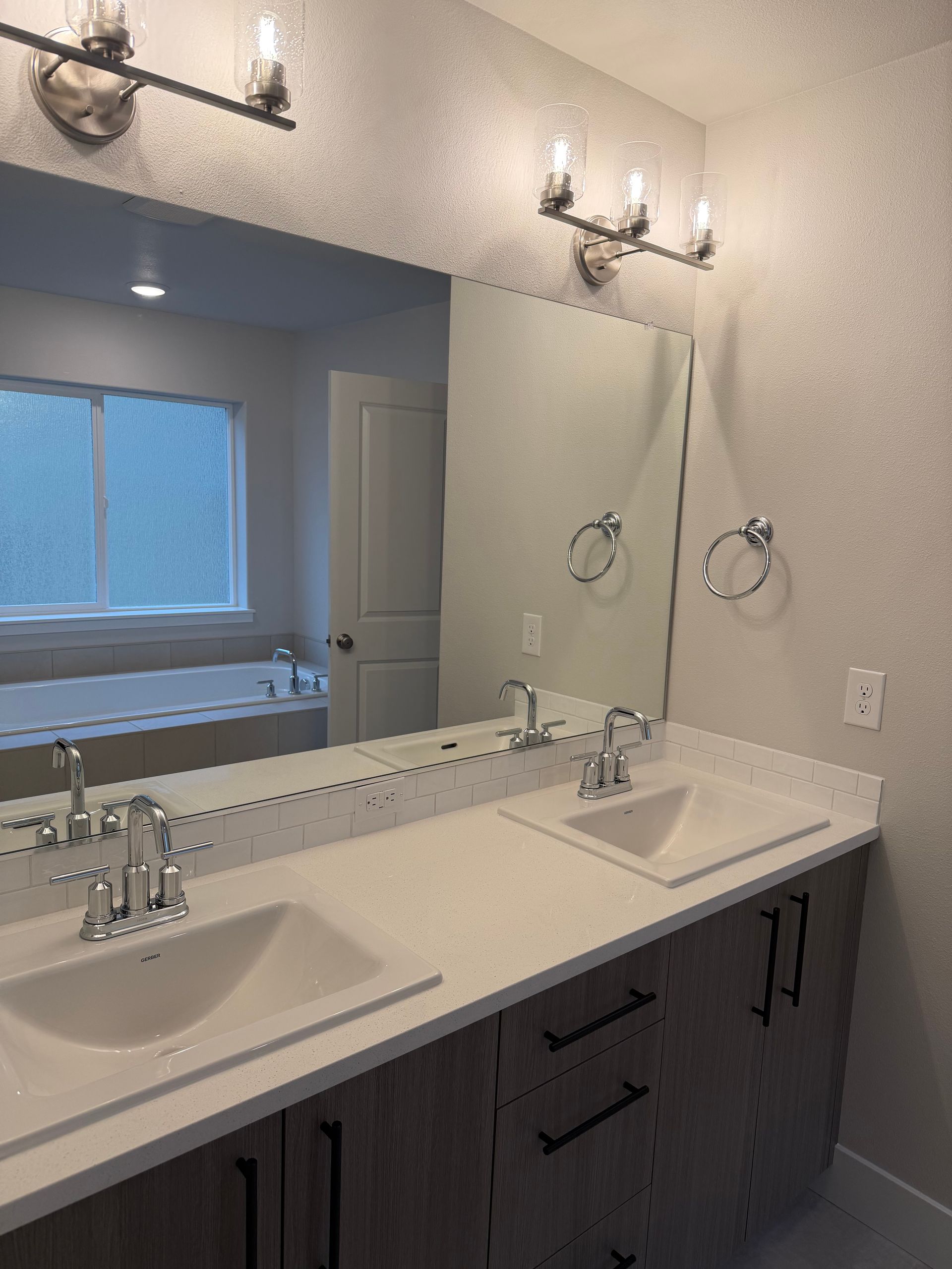 Bathroom with double sink vanity, large mirror, and wall sconces.
