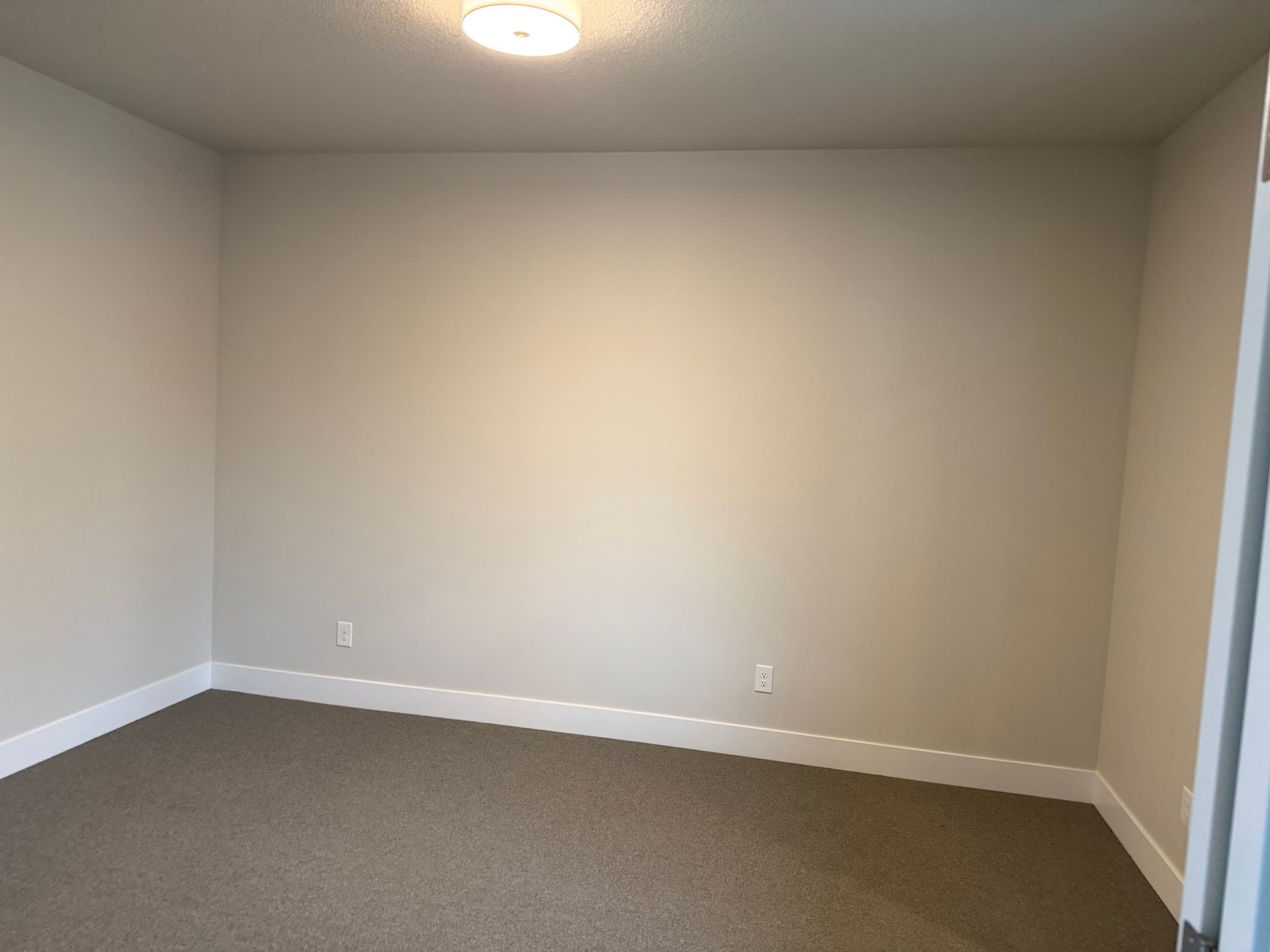 Empty room with beige walls, brown carpet, and white trim. Ceiling light.