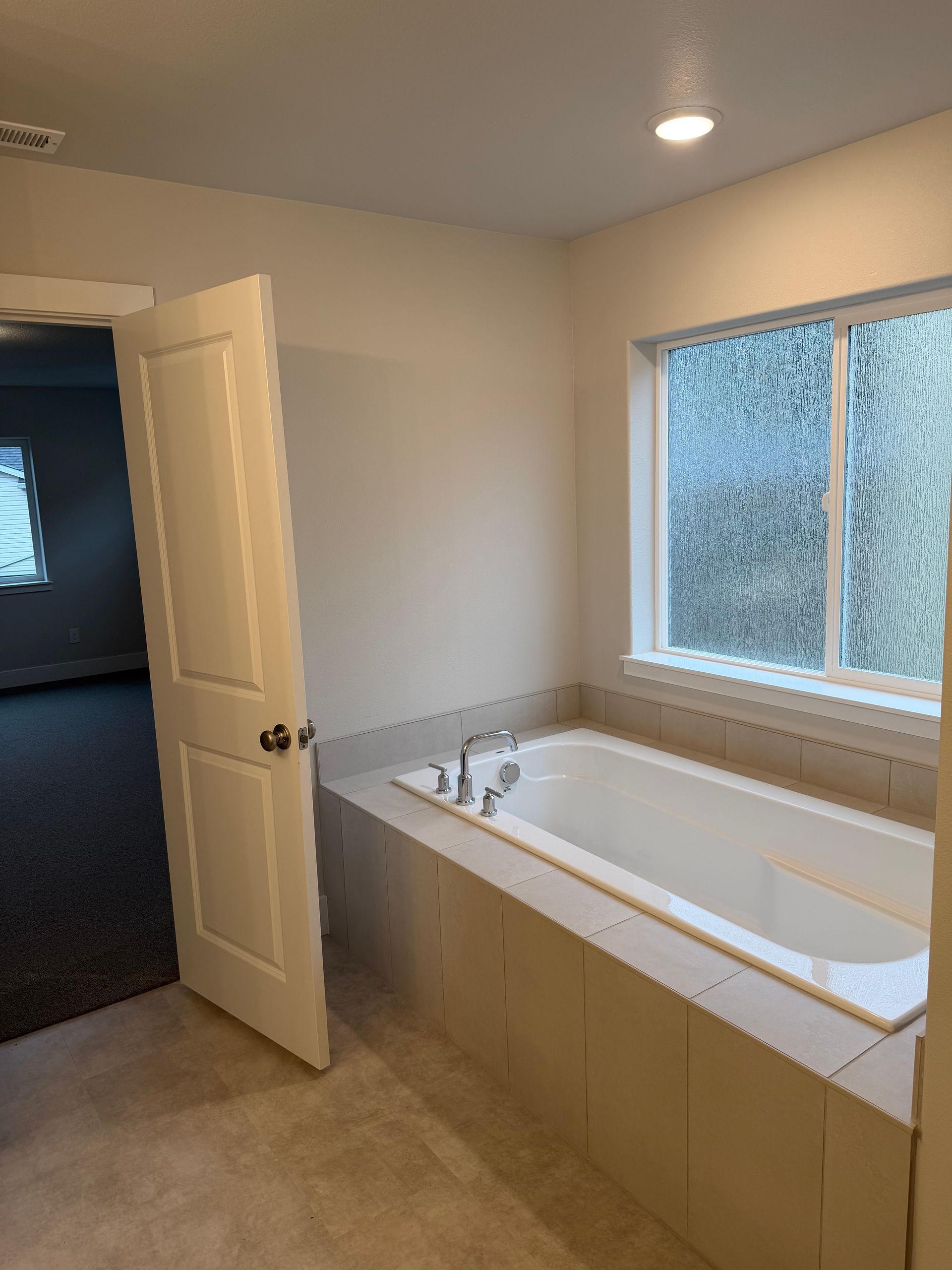 Bathroom with built-in bathtub. White walls, tile surround, window with frosted glass. Doorway to another room visible.