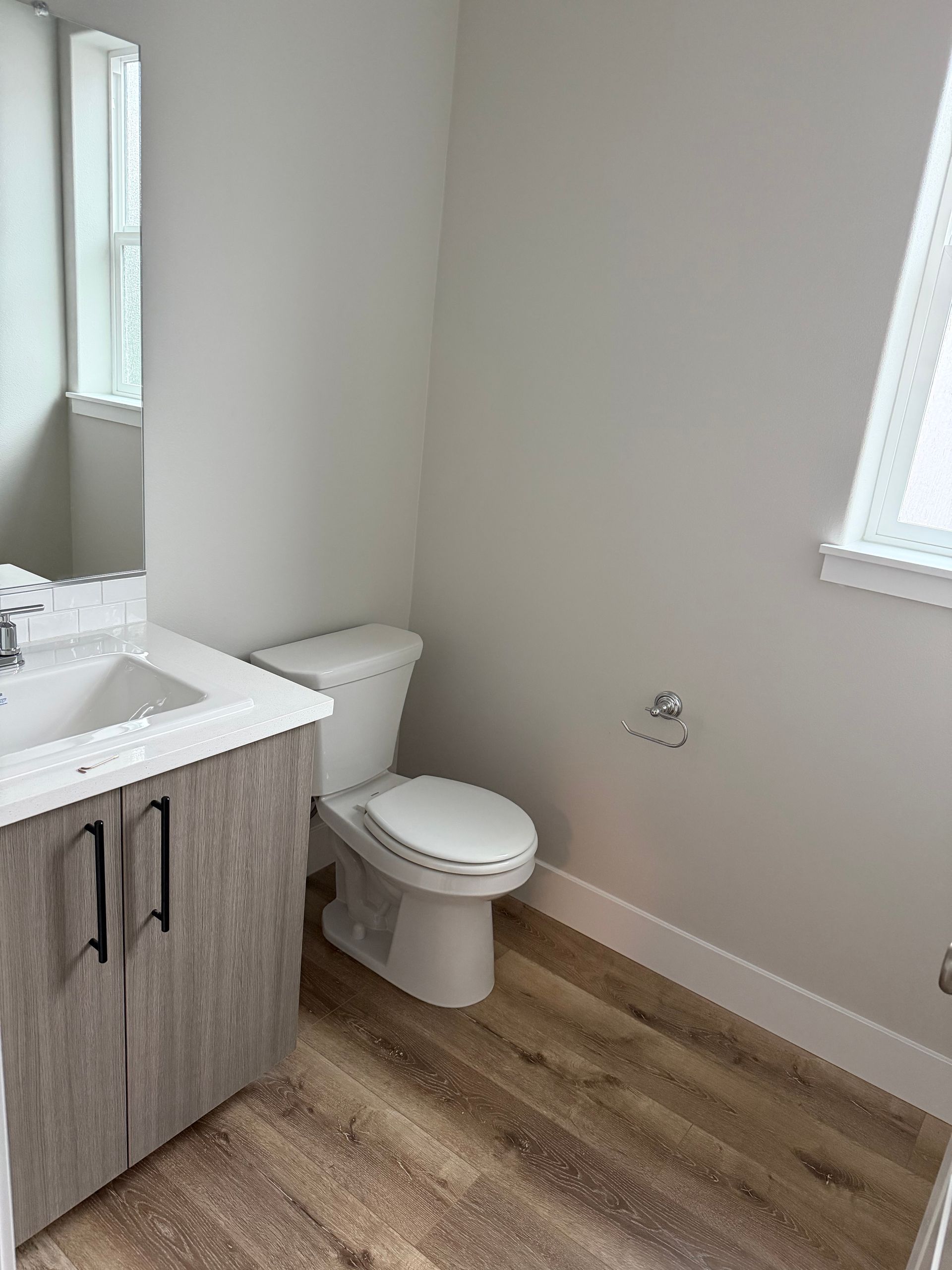 Bathroom with toilet, vanity, and window; gray walls, wood-look floor.