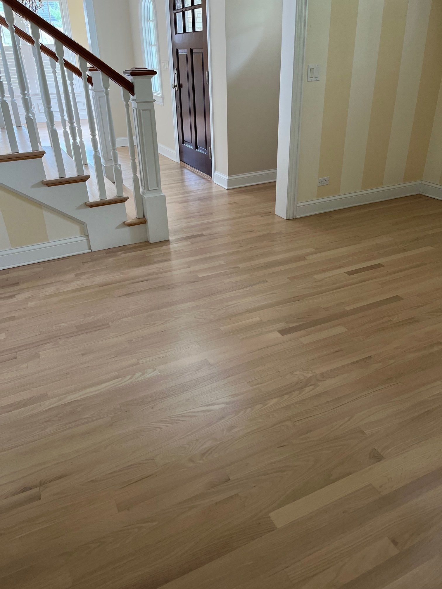 Hardwood floors lead to a staircase and door. Light walls and tan/gold vertical striped wall are visible.