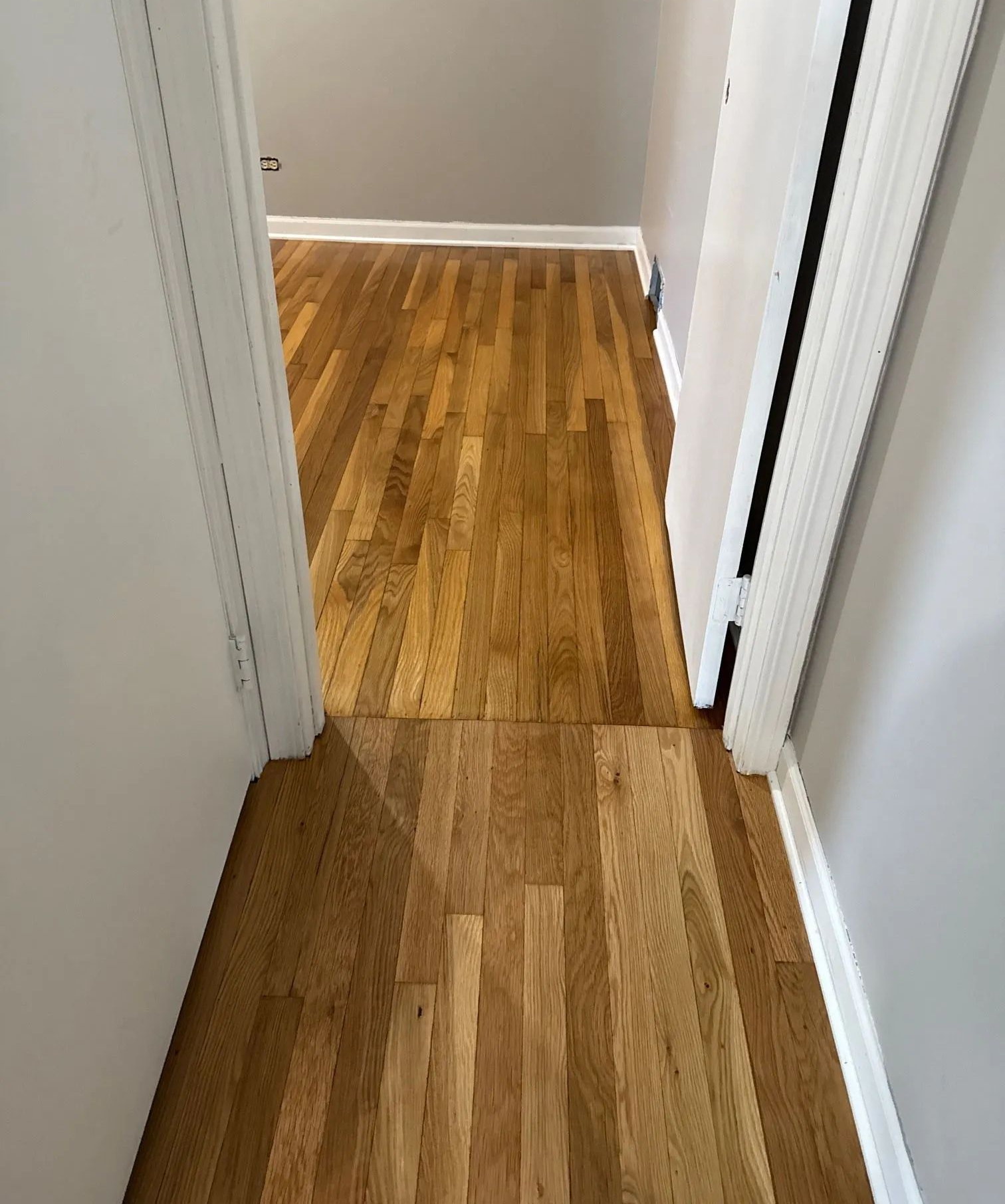 Narrow hallway with light wood flooring and white walls, viewed from above.