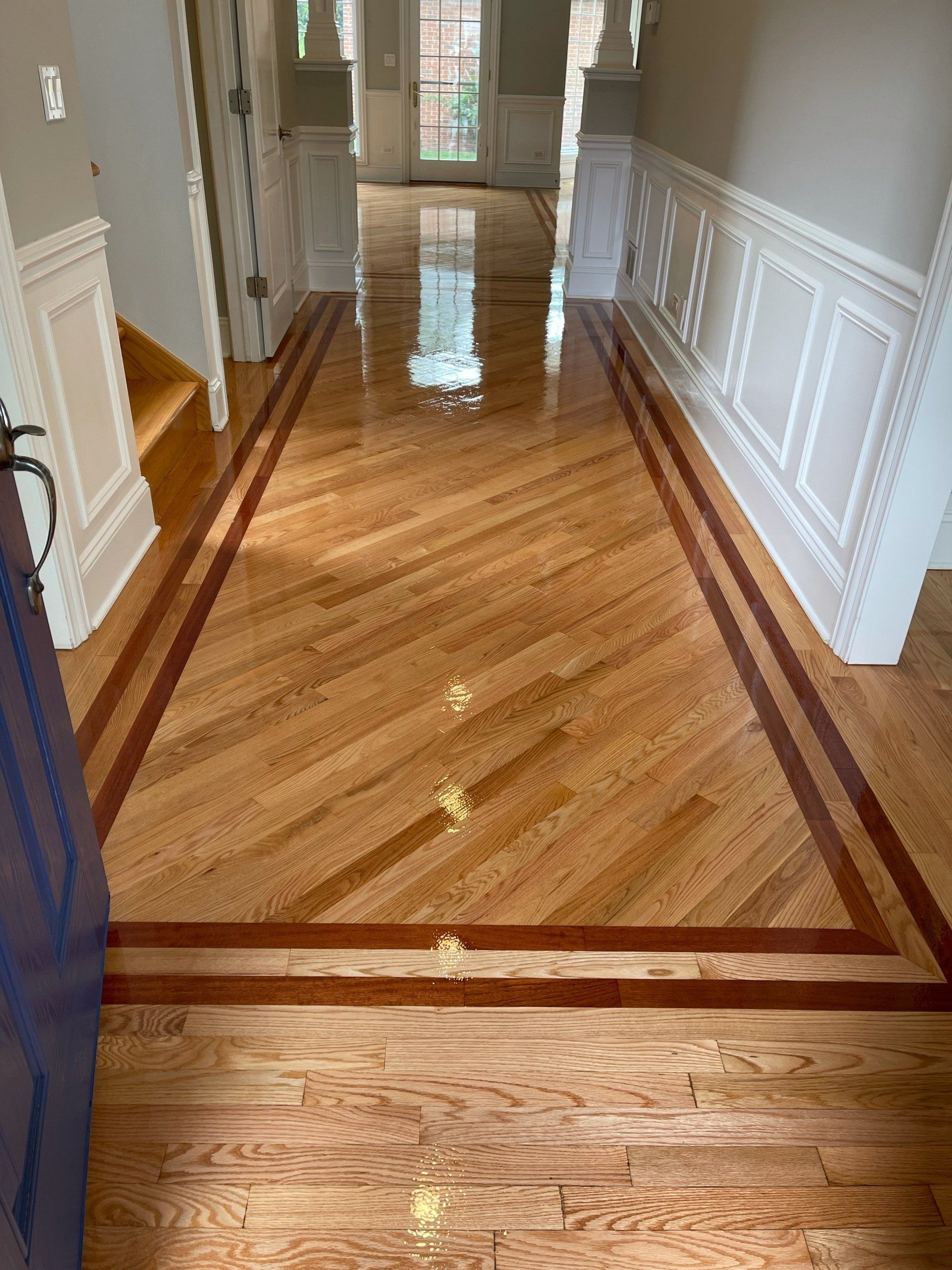 Wooden hallway with herringbone pattern floor bordered by dark wood and white wainscoting.