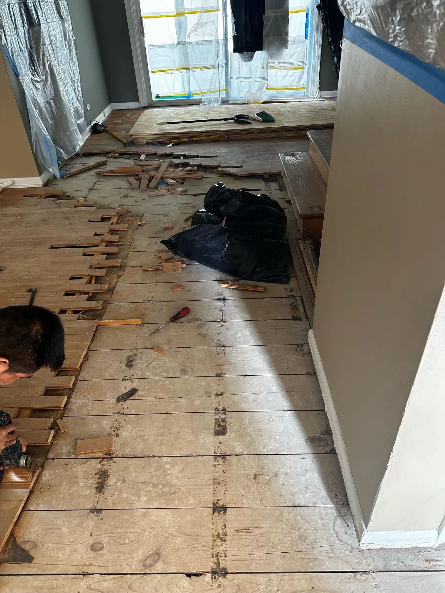 A person using a tool to remove old wood floor planks from a subfloor in a room undergoing home renovations.