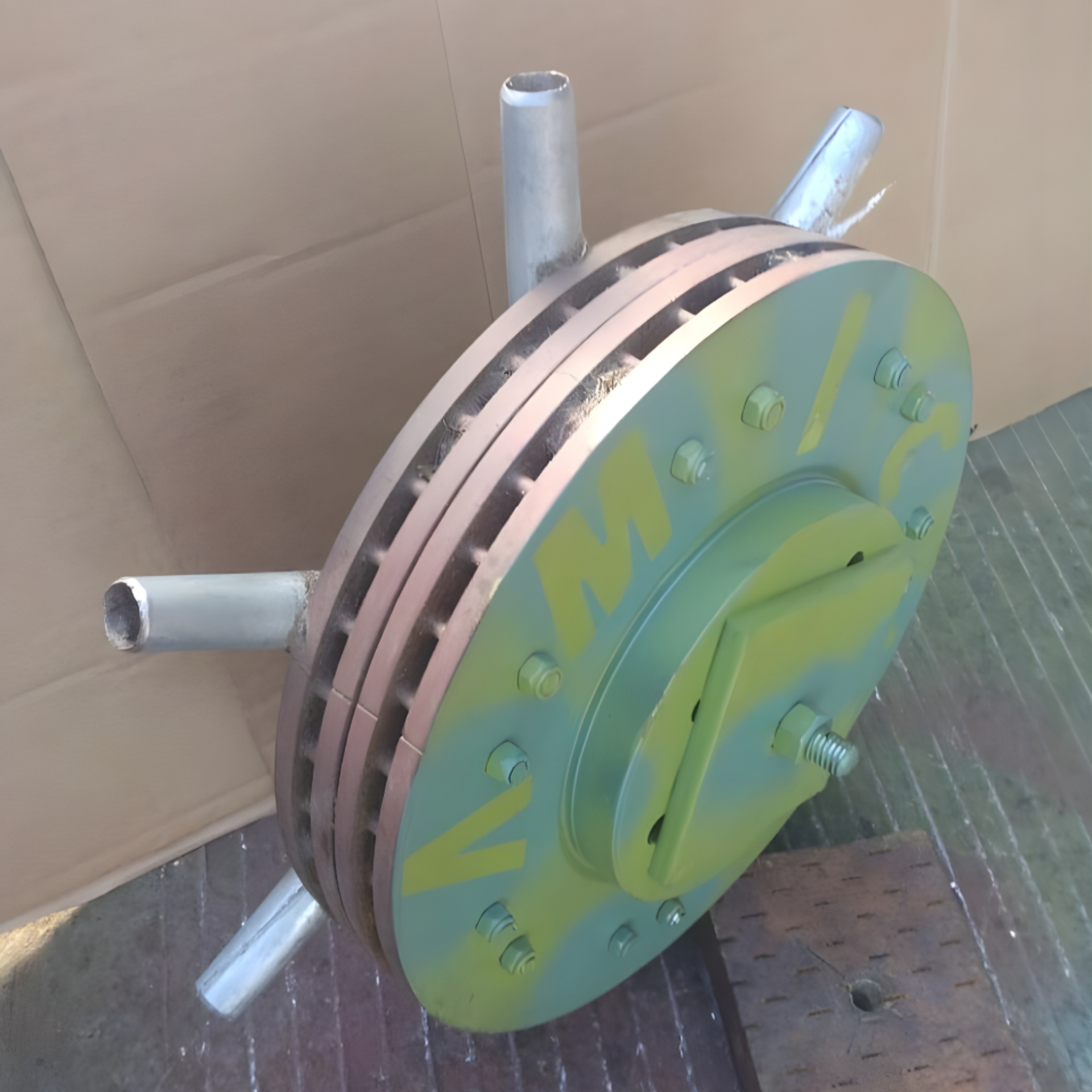A vented, circular metal brake disc with green paint and three protruding metal tubes attached to its edge.