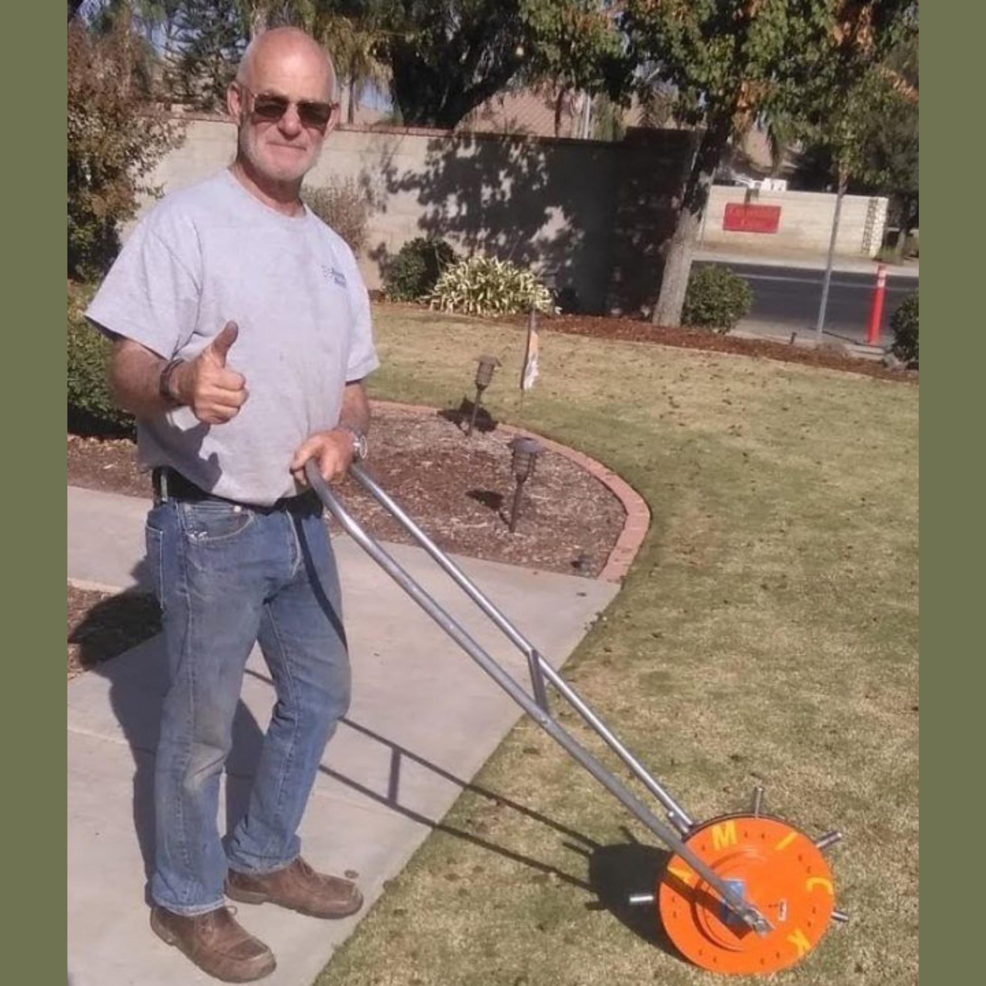 A person stands on a sidewalk, giving a thumbs up while holding a rolling measuring wheel on a grassy lawn.