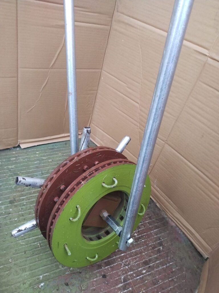 A custom-made tool featuring two rusty circular brake rotors and a painted green metal disc mounted on a metal frame.