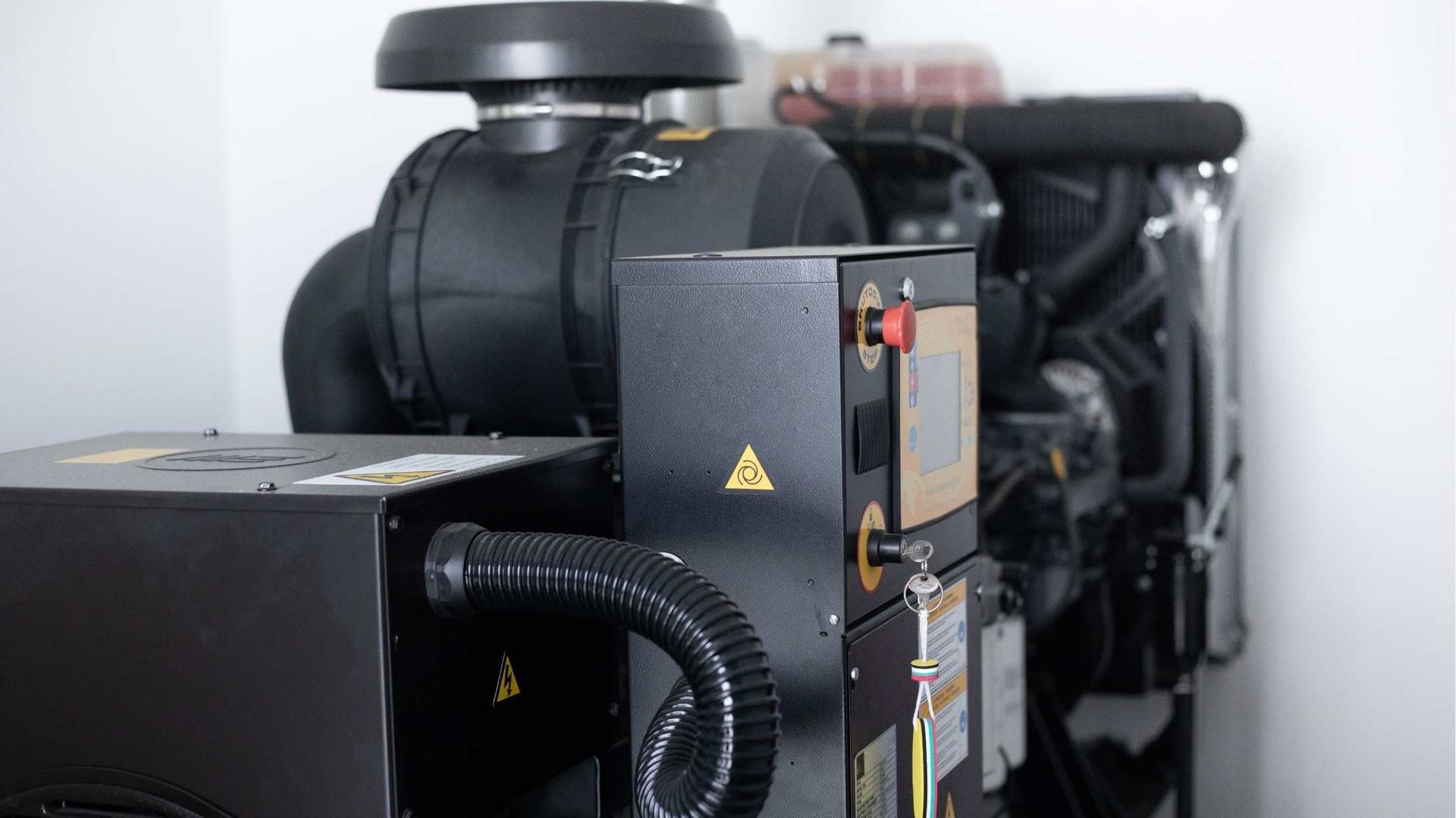 A black industrial generator with a control panel, prominent emergency stop button, and air intake housing.