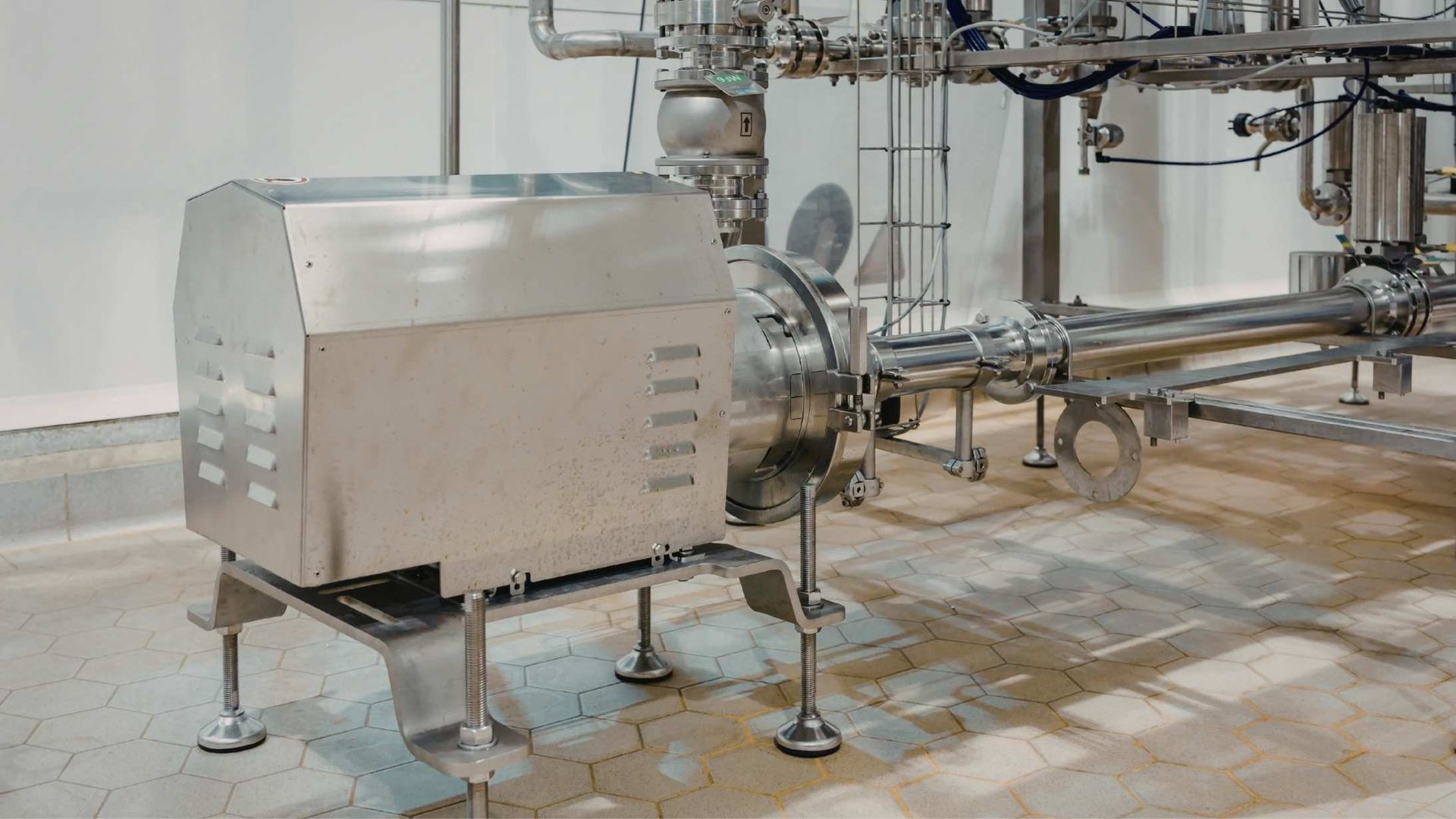 Stainless steel industrial pump and piping system mounted on legs in a clean facility.